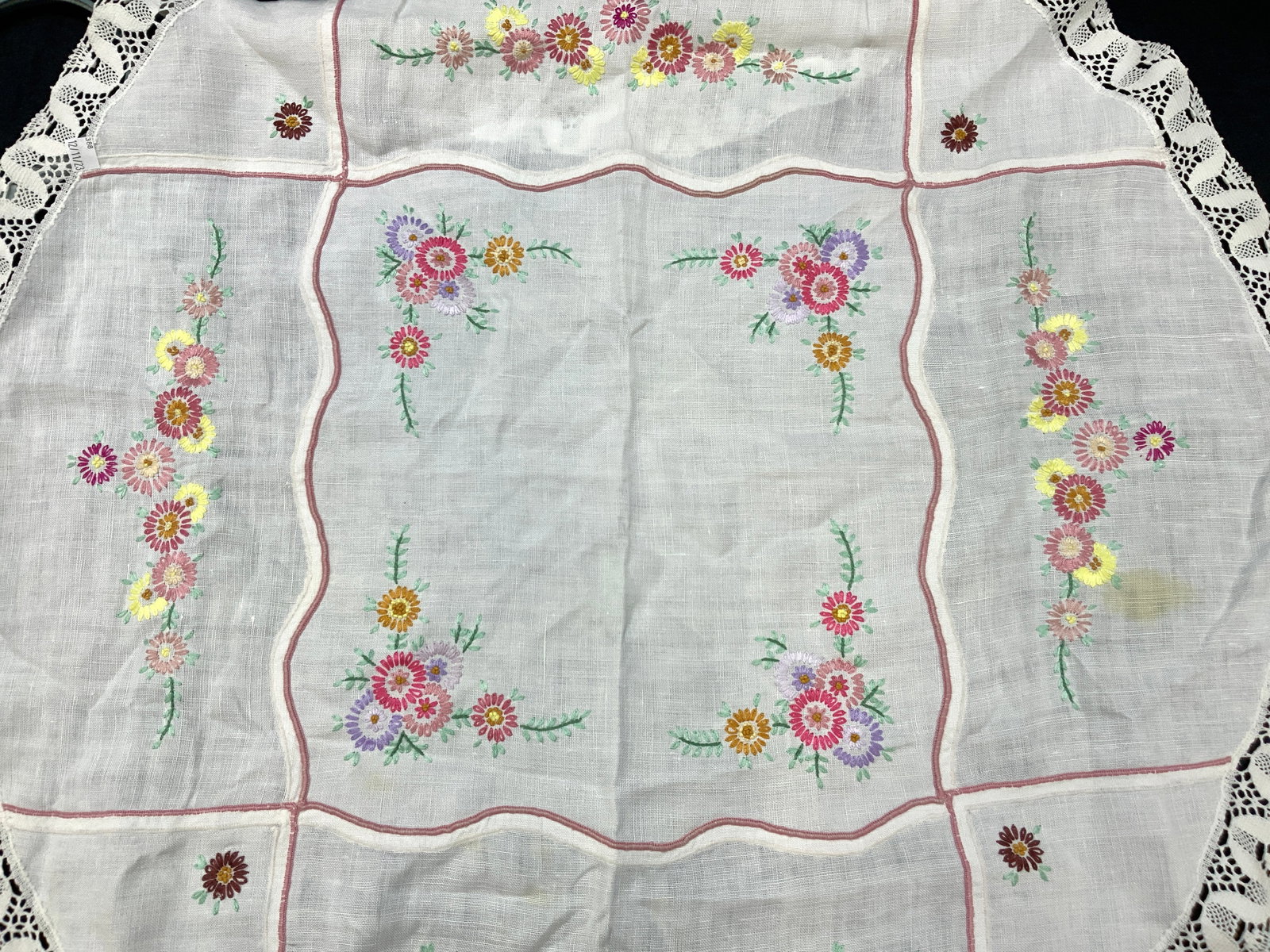 Embroidered Floral Circular Linen Tablecloth: White toned linen tablecloth in a circle with hand embroidered floral designs on all sides and lace outer edges. Approx 3ft x 3ft Evident blemishes to linen. Embroidered linens. Linen tablecloth, tabl