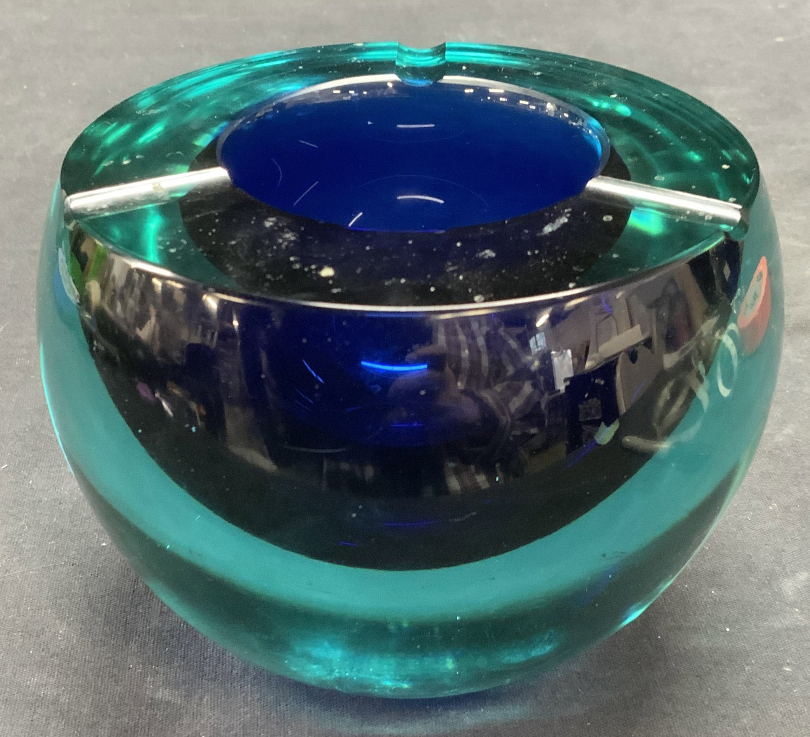 Teal to Cobalt Blue Heavy Art Glass Bowl: Teal to cobalt blue toned art glass bowl/ashtray. Indented on rim. Thick walled glass. Piece is heavy. Measures approx. 5 x 4 inches. Some scratching observed. Art glass, art glass bowl, art glass ash