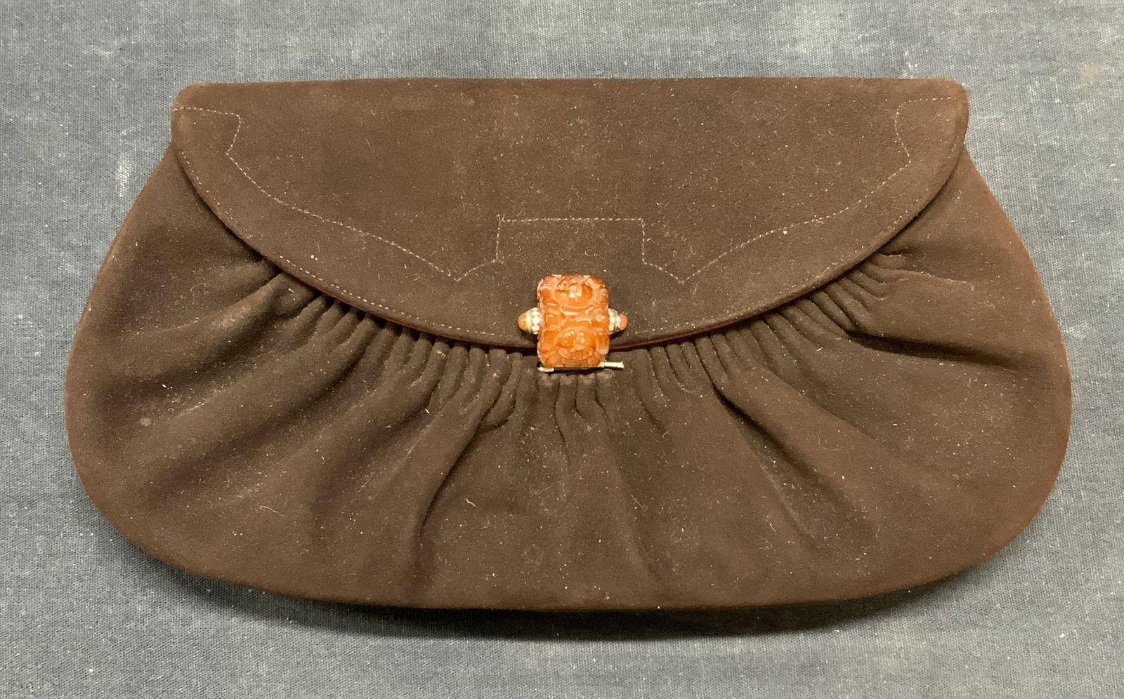 Vintage Nettie Rosenstein Brown Suede Clutch: Vintage Nettie Rosenstein brown suede clutch. Ruched front design with sculptural carved floral amber lucite clasp. Satin lining with 2 slip pockets to interior. Designer label to interior. Measures a