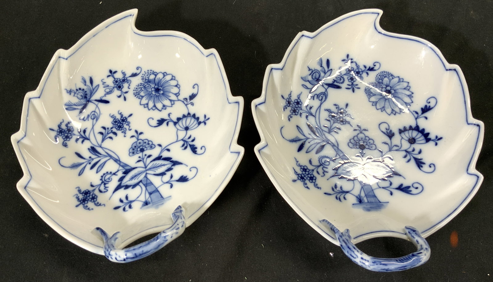 MEISSEN Pair Porcelain Leaf Plates: Undersides are marked MEISSEN. Each are porcelain. Plates are each white with blue toned floral, & leaf detail. Each piece has stem shaped handles at ends. Each measures approximately 8.5 inches long 