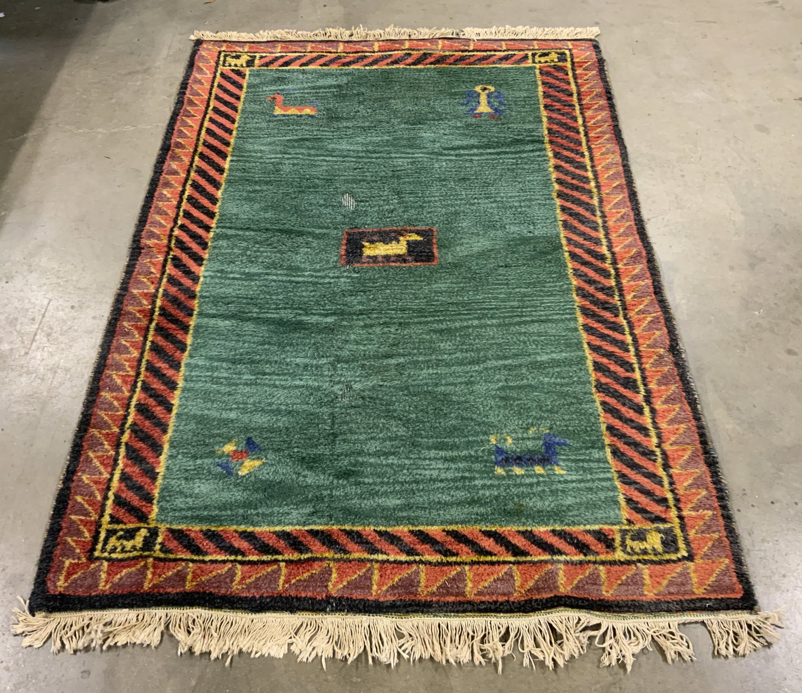 Vintage Fringed Handmade Wool Pile Area Rug: Rug is handmade and wool. Piece has geometric detail near edges. Rug also has geometric style animal figure detail. Edges of rug have cream toned fringes. Rug measures approximately 75 inches long 50 