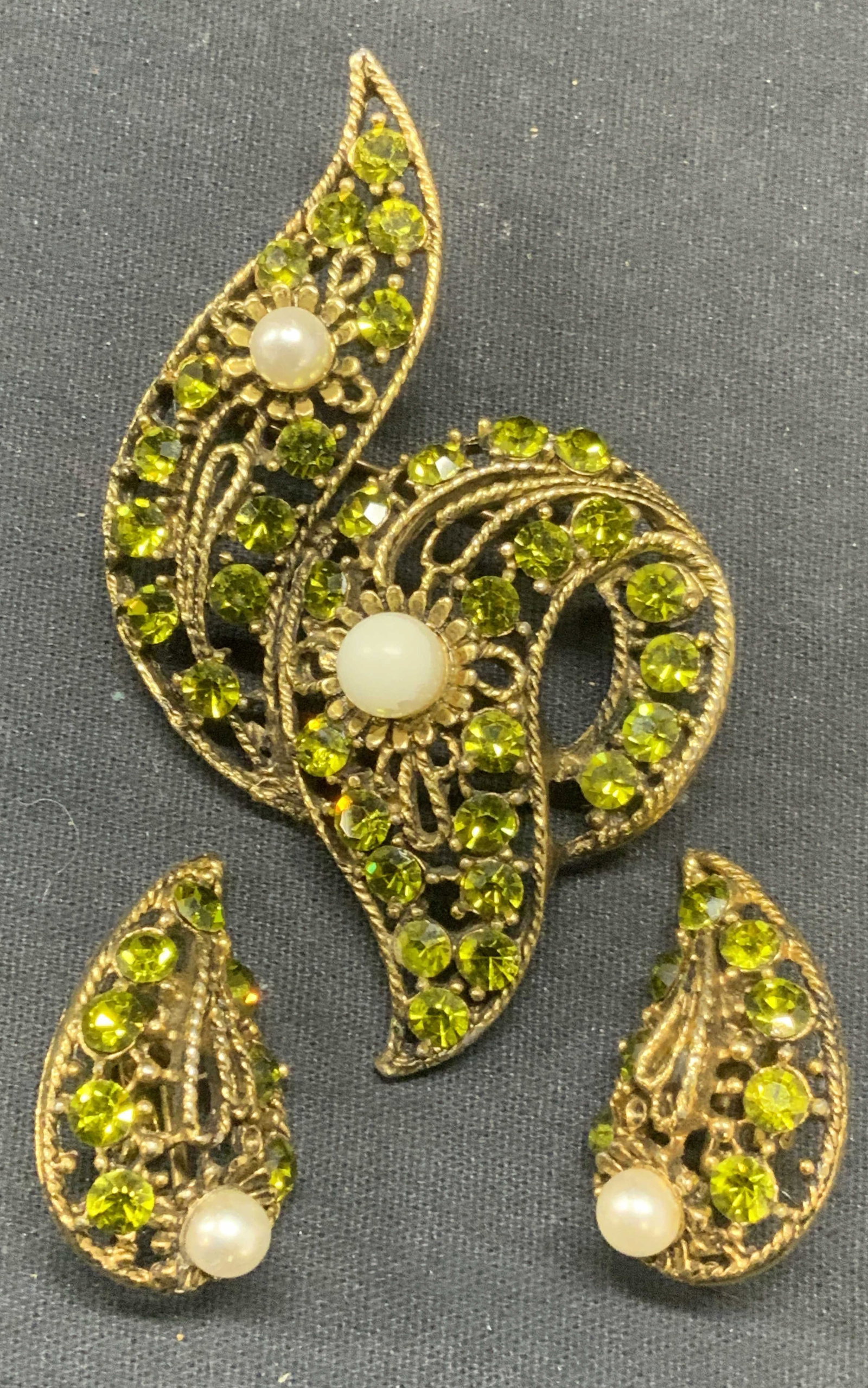 Vintage Gold Tone Green Crystal Brooch & Earrings: Vintage matching gold tone brooch and clip on earring set. Faux pearl and green decoration. Brooch measures approx. 3 x 2 inches. Earrings measure approx. 1.25 x .75 inches. Both pieces have some surf