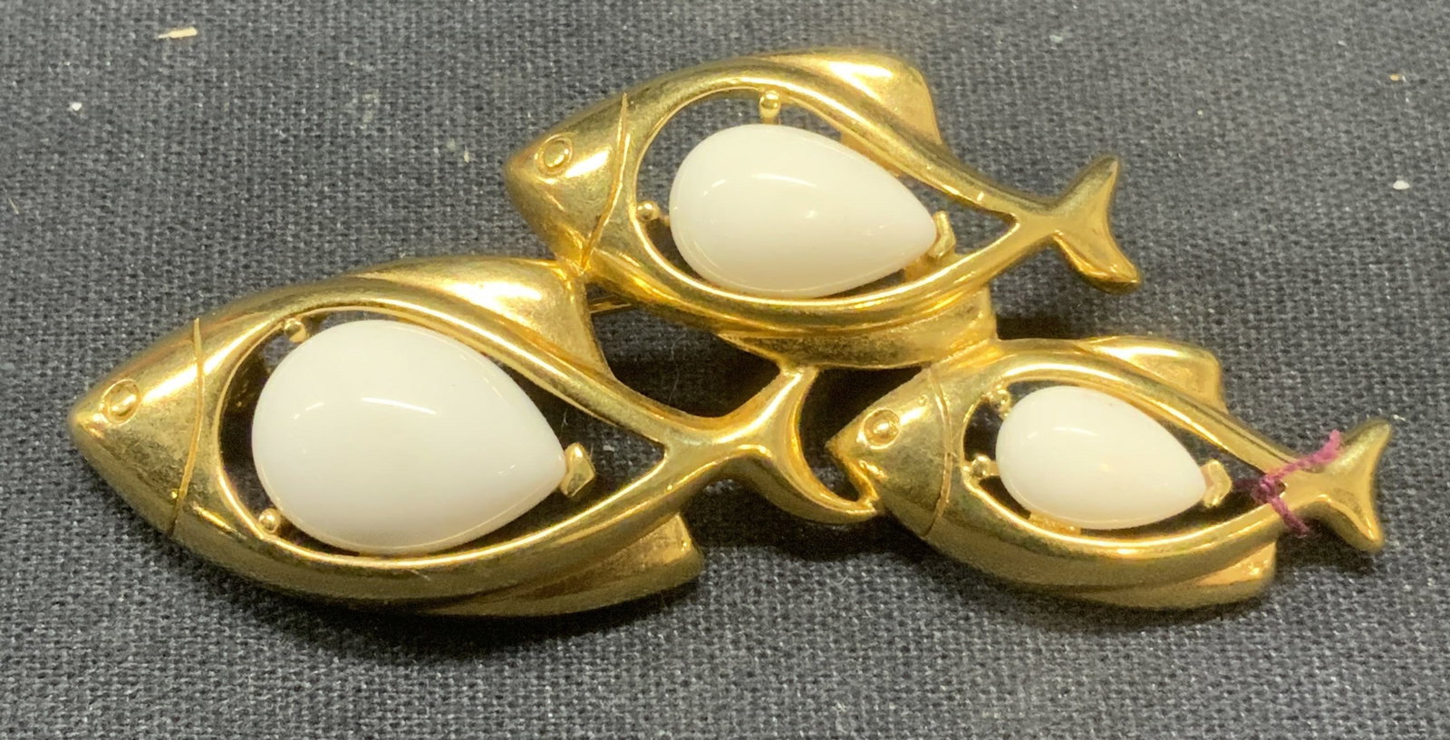 Vintage Trifari Gold Tn White Lucite Fish Brooch: Vintage Trifari gold tone school of fish brooch with white drop shaped lucite Cabochon decoration. Signed to underside. Hinge pin to underside. Measures approx. 2.5 x 1.5 inches. Some surface wear inc