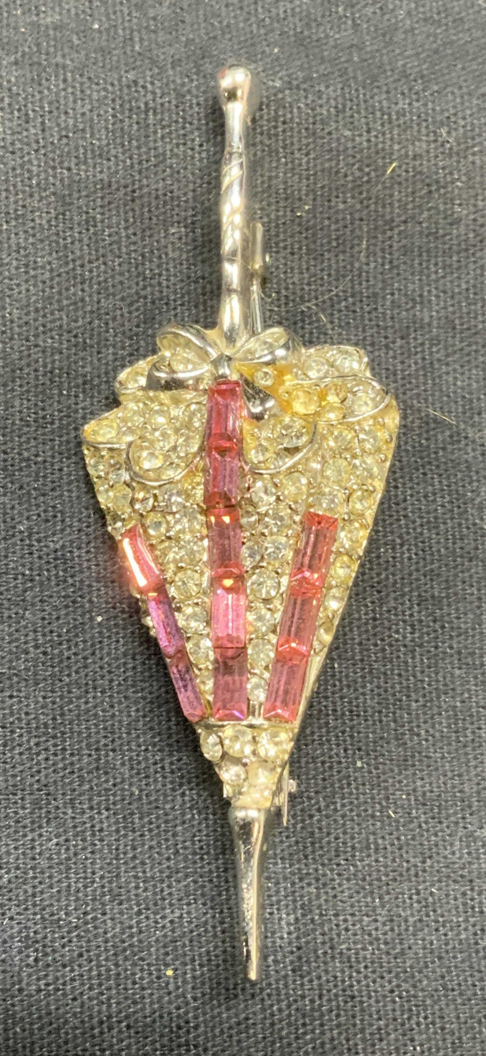 Vintage Silver Tn Pink Crystal Umbrella Brooch: Vintage silver tone umbrella shaped brooch with pink and colorless crystal decoration. Hinge pin to underside. Measures approx. 2.75 x 1 inches. Some surface wear including scratching observed. Estate