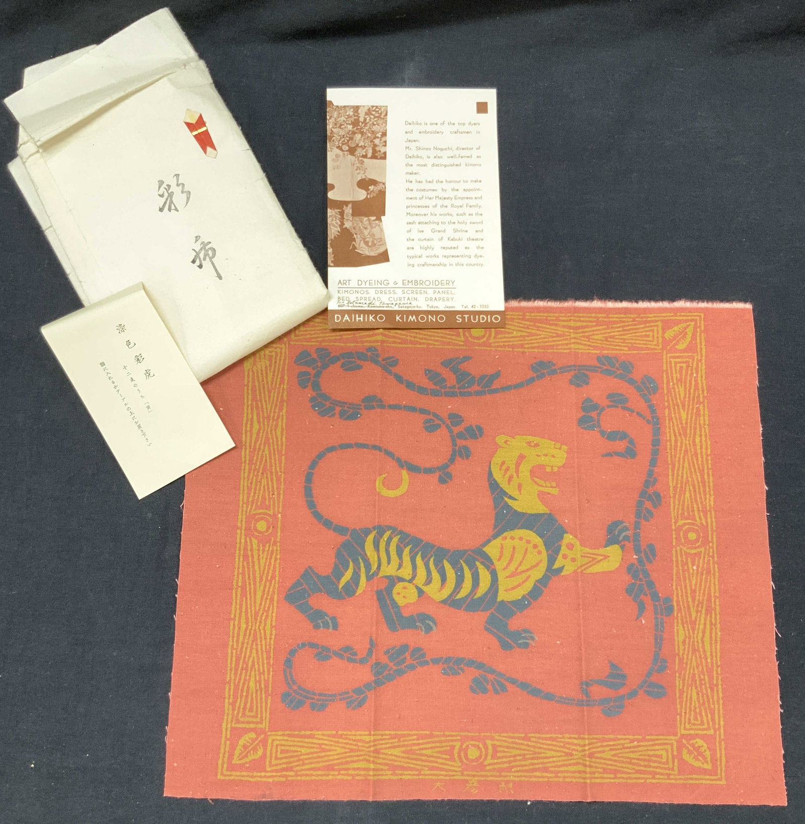 Shinzo Noguchi Hand Dyed Japanese Textile: Hand dyed textile panel that depicts a tiger in dark blue and gold toned patterns with blue vines and gold toned accent patterns on boarder on top of a red base. Comes with papers in Japanese that rea