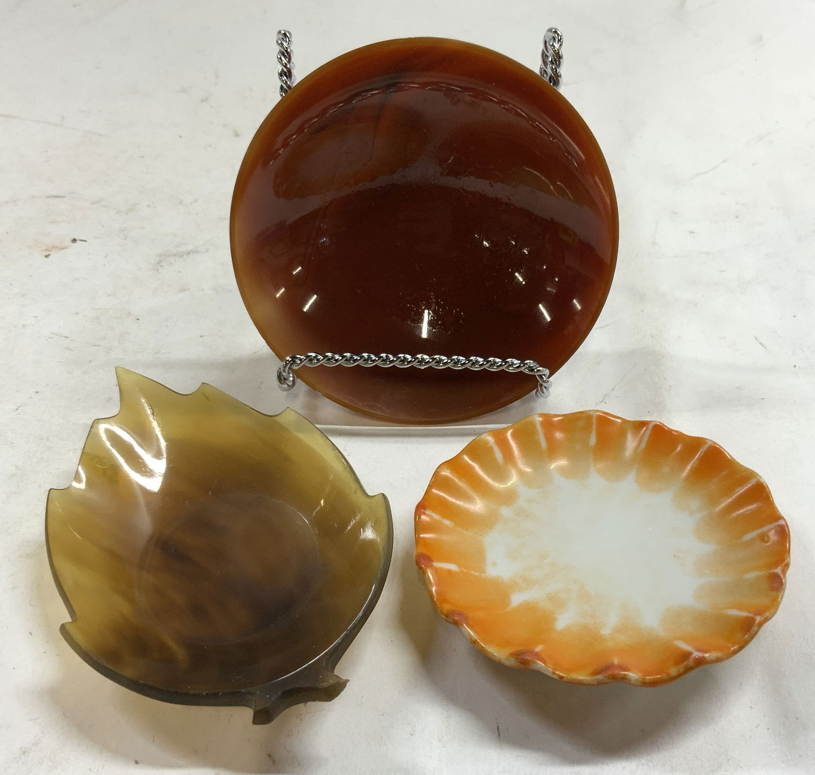Lot 3 Glass & Porcelain Trinket Dishes: Lot includes 3 trinket dishes. One circular shaped glass dish, one leaf shaped dish which appears to possibly be Bakelite, & 1 porcelain trinket dish with ruffled edges. Largest trinket dish measures