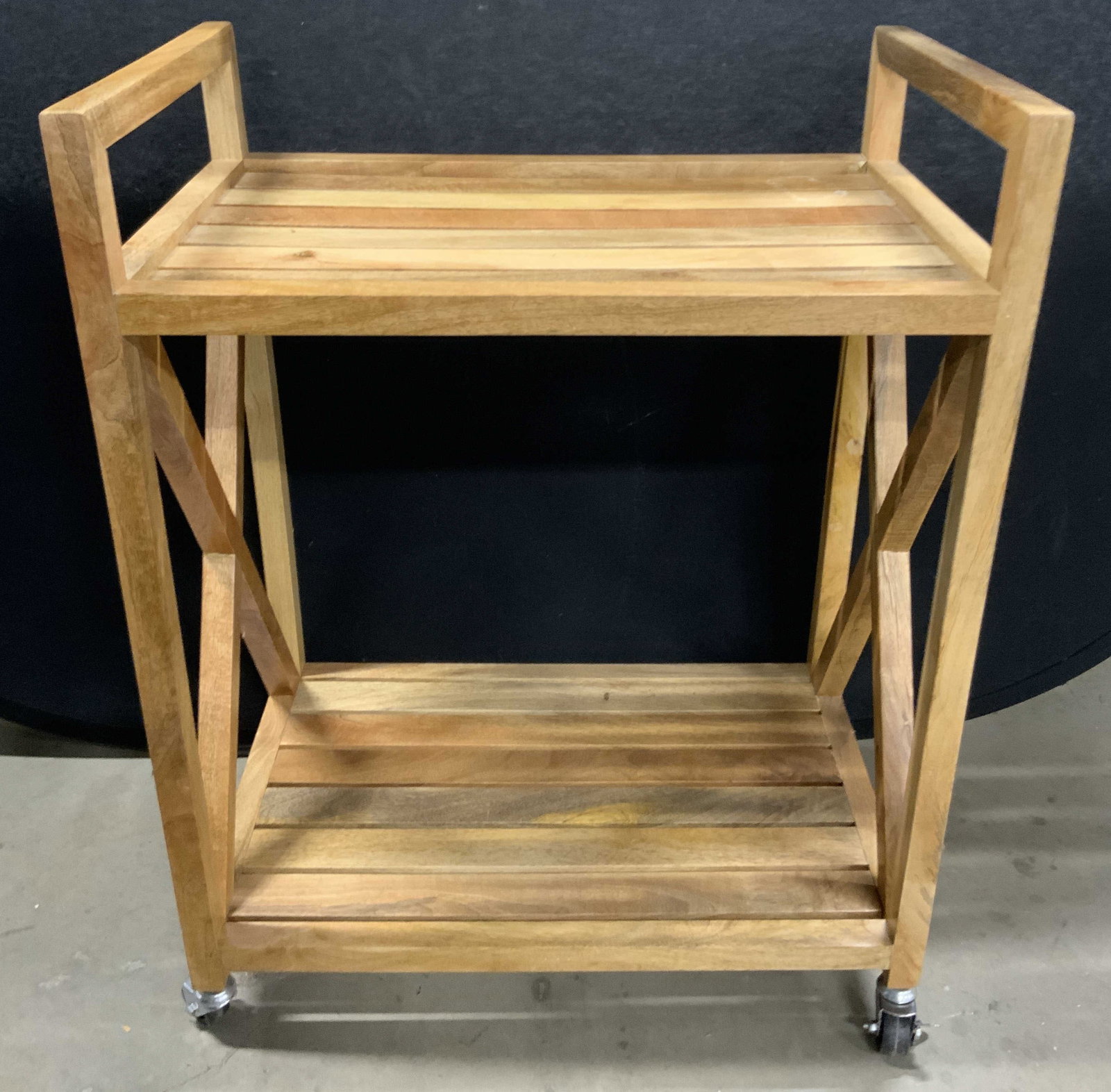 TARGET BRANDS Two Tier Wheeled Wooden Bar Cart: A two tier wheeled wooden bar cart with X shaped stretchers. Four wheels to the underside. Crafted from light brown hued wood. Measures approx. 36H x 28D x 18W in. Underside sticker reads 2015 TARGET 