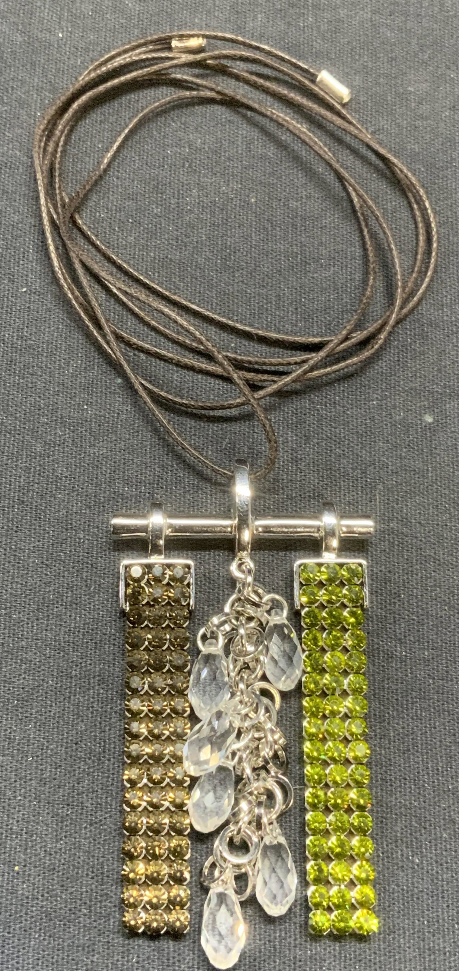 Green & Colorless Crystal Pendant Necklace: Necklace with brown cord and silver tone pendant. Green and colorless crystal decoration. Drop length approx. 17 inches. Pendant measures approx. 1.5 x 2.25 inches. Some scratching observed. Estate je