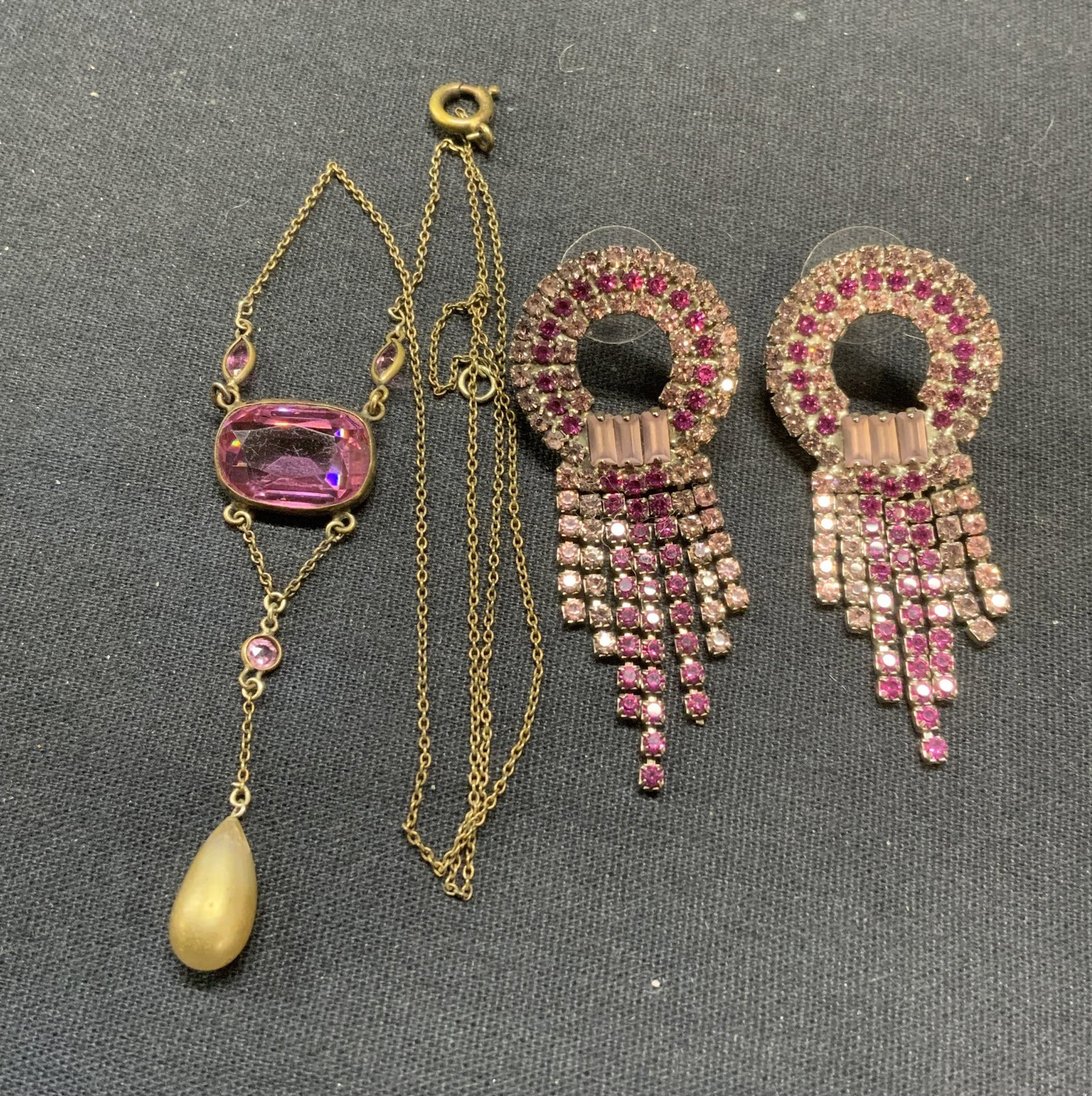 Lot 2 Pink Crystal Earrings & Pendant Necklace: Lot of 2 jewelry pieces. Open circle pink crystal decorated dangle earrings. Post backing. Measures approx. 2 1/8 x 7/8 inches. Gold tone pendant necklace with pink crystal and faux pearl decoration. 