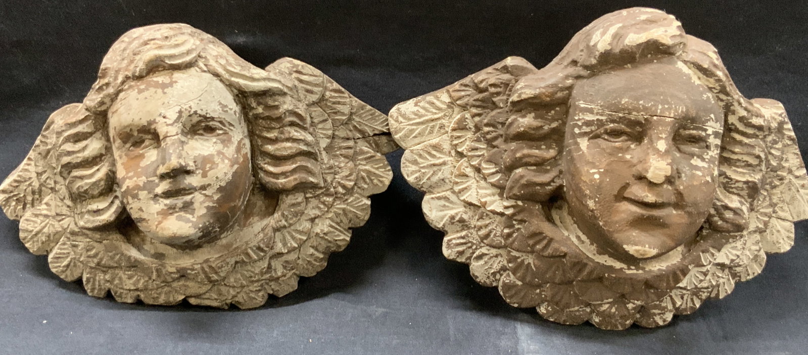 Pr Carved Wooden Angel Head Accessories: Pair of carved wooden angel heads, depicting the heads of men with angel wings around the head. Approx 7.5 inches tall and 9.5 inches wide. Evident wearing to paint job of heads and cracking and losse