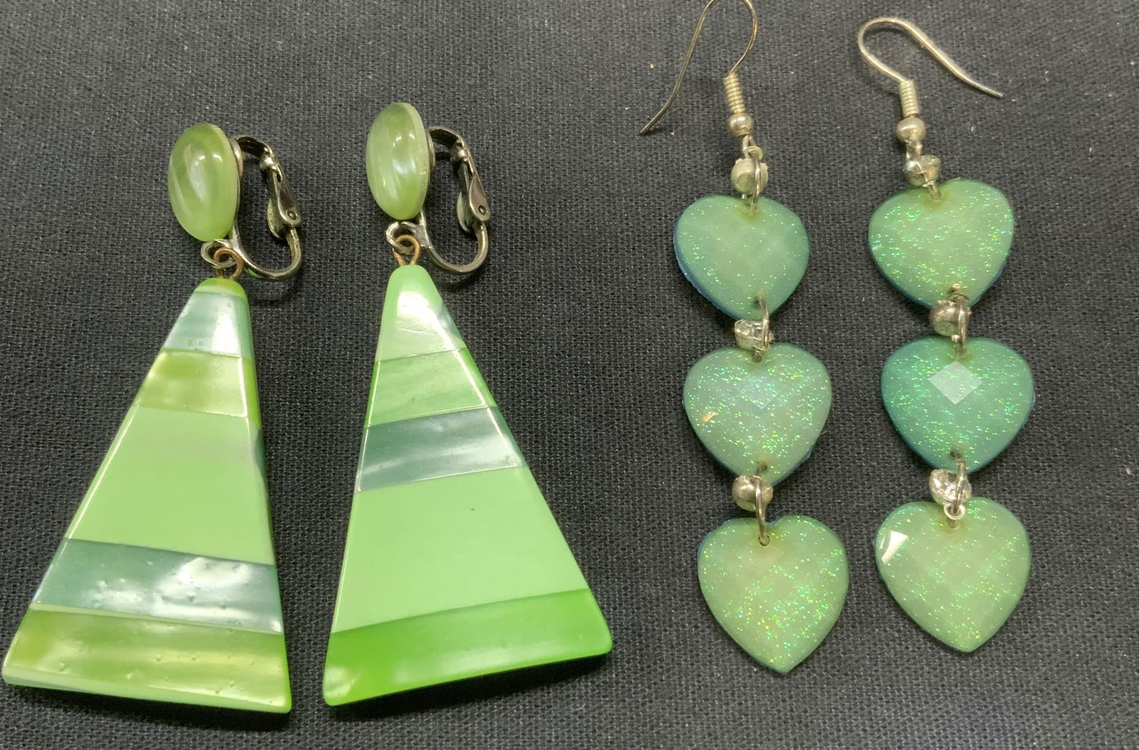 Lot 2 Green Lucite Dangle Earrings: Lot of 2 jewelry pieces. Sparkly green lucite heart shaped dangle earrings. Hook backing. Measure approx. 2.25 inches long. Green striped lucite triangular dangle earrings. Clip on backing. Measure ap