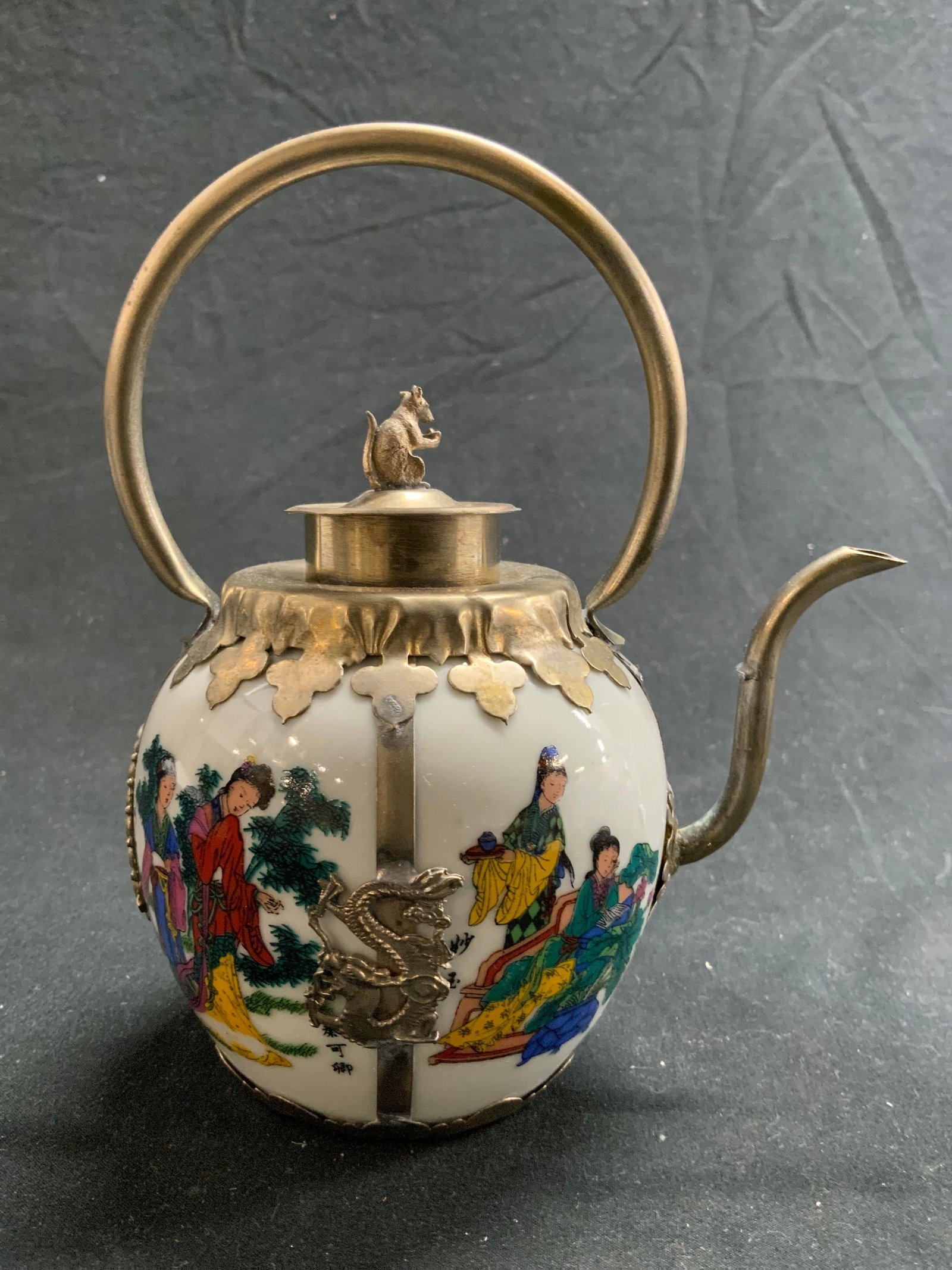 Hand Crafted Porcelain Asian Teapot Rat Finial: Asian teapot with Hand painted porcelain in white with Asian ladies dressed in traditional clothing. . Tibetan metal handiwork featuring Chinese dragons and a rat figurine finial., total depth 5.25 in