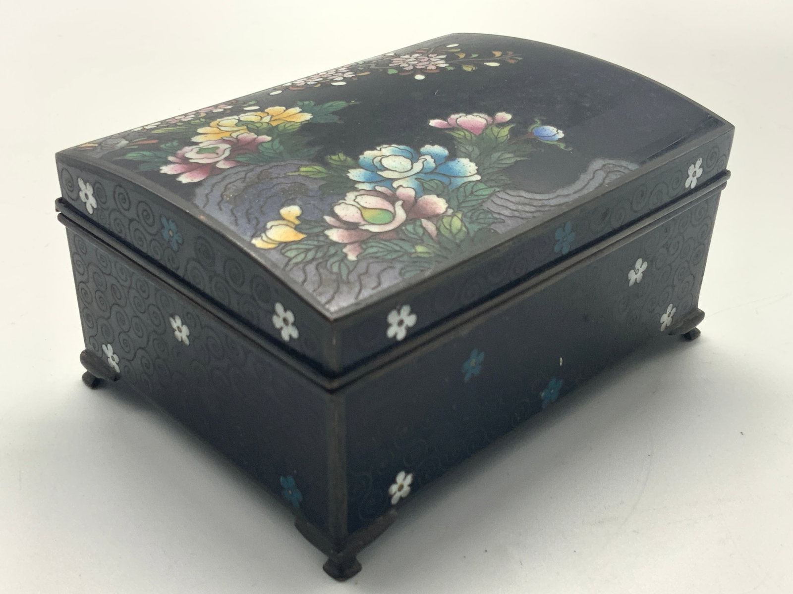 Vintage Cloisonne Asian Music Box, Japan: Vintage cloisonne Asian music box with black base with spiral deigns and floral enamel motifs on sides and lids. Interior is lined with silver toned metal and 1 section has hidden mechanics for music 
