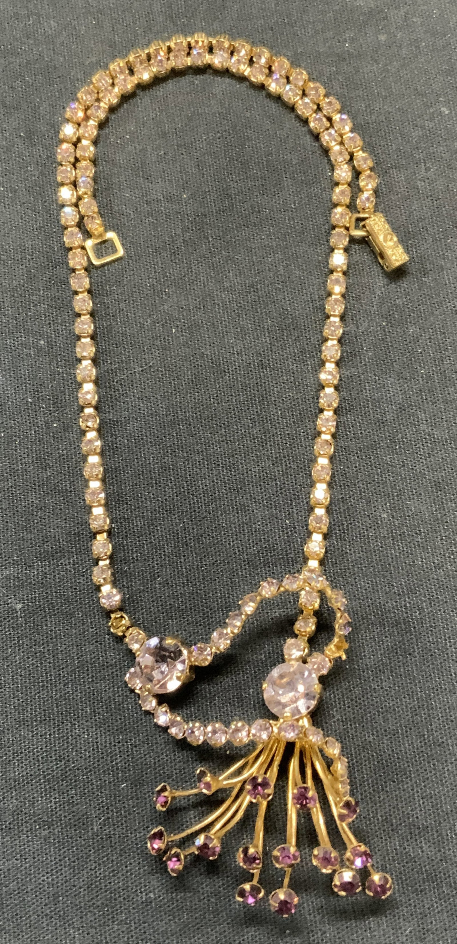 Vtg Gold Tn Purple Crystal Pendant Necklace: Vintage gold tone pendant necklace with purple crystal decoration. Drop length approx. 7 inches. Pendant measures approx. 1.75 x 1.5 inches. Some surface wear including scratching observed, some cryst