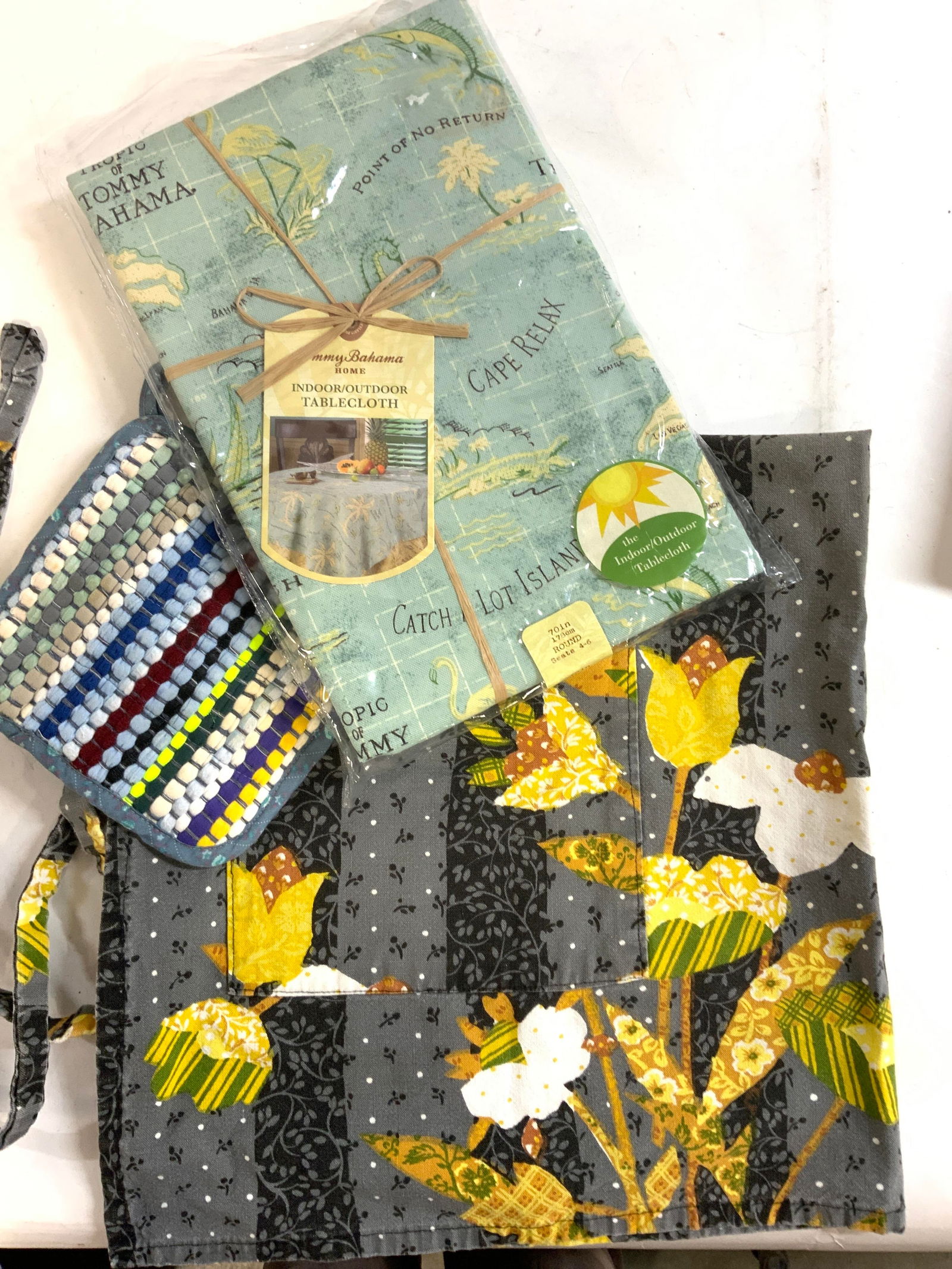 3 Tommy Bahama NIP Tablecloth, Apron, Pot Holder: Indoor/ outdoor Tommy Bahama Round Tablecloth , 70 in. diameter., tropical motif with palm trees., new in package. Cotton waist apron , grey and black with yellow and white flowers. 2 large pockets. 2