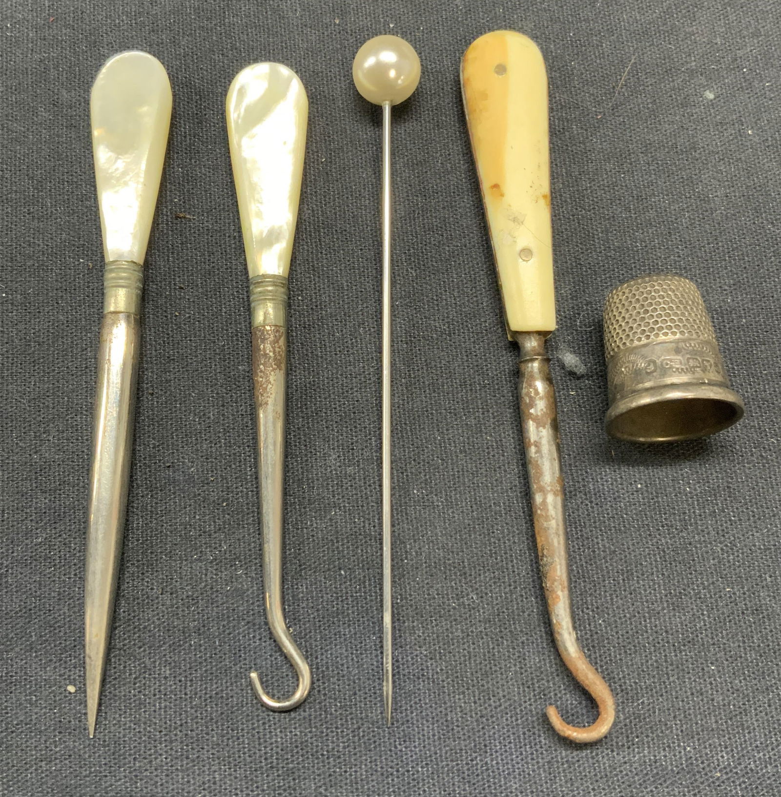 5 Button Hooks, Hat Pin, Sterling Sliver Thimble +: Group lot of vintage and possibly antique home accessories. Sewing awl and button hook with mother of pearl handles. Button hook with bone handle. Faux pearl beaded pin. Sterling silver thimble with s