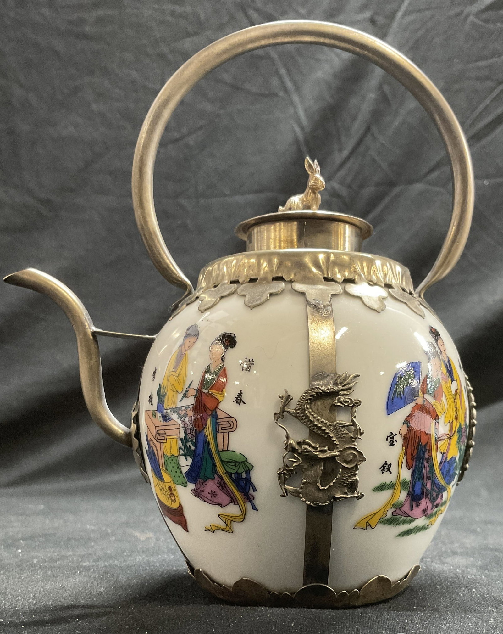 Handcrafted Porcelain Asian Teapot: Asian teapot with Hand painted porcelain in white with Chinese figures. Tibetan metal handiwork featuring Chinese dragons and rabbit figurine finial., total width 4.75 in. Total height 6 in. Asian dec