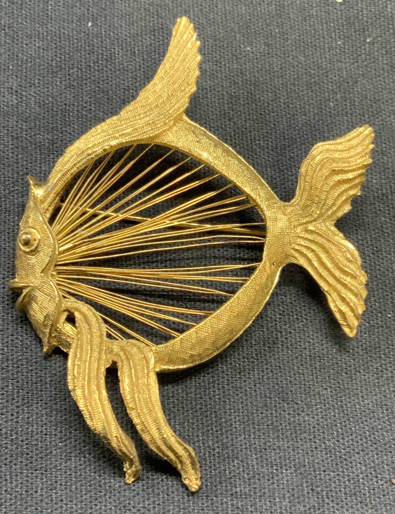 Vintage Monet Gold Tone Fish Brooch: Vintage Monet gold tone fish brooch with textural body and wire detail. Signed to underside. Hinge pin to underside. Measures approx. 2.5 x 2 inches. Some surface wear including scratching observed. E