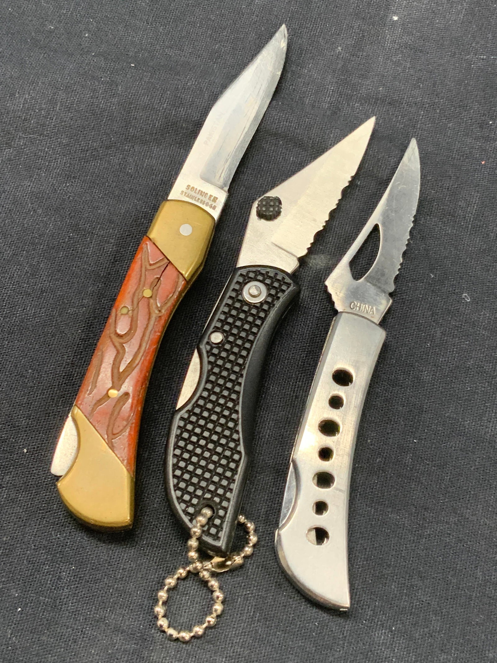 Lot 3 Stainless Steel Pocket Knives: Lot of 3 stainless steel pocket knives. All marked stainless steel. 1 chrome toned metal handle with serrated blade another with an acrylic made handle, also with a serrated blade and another with bea