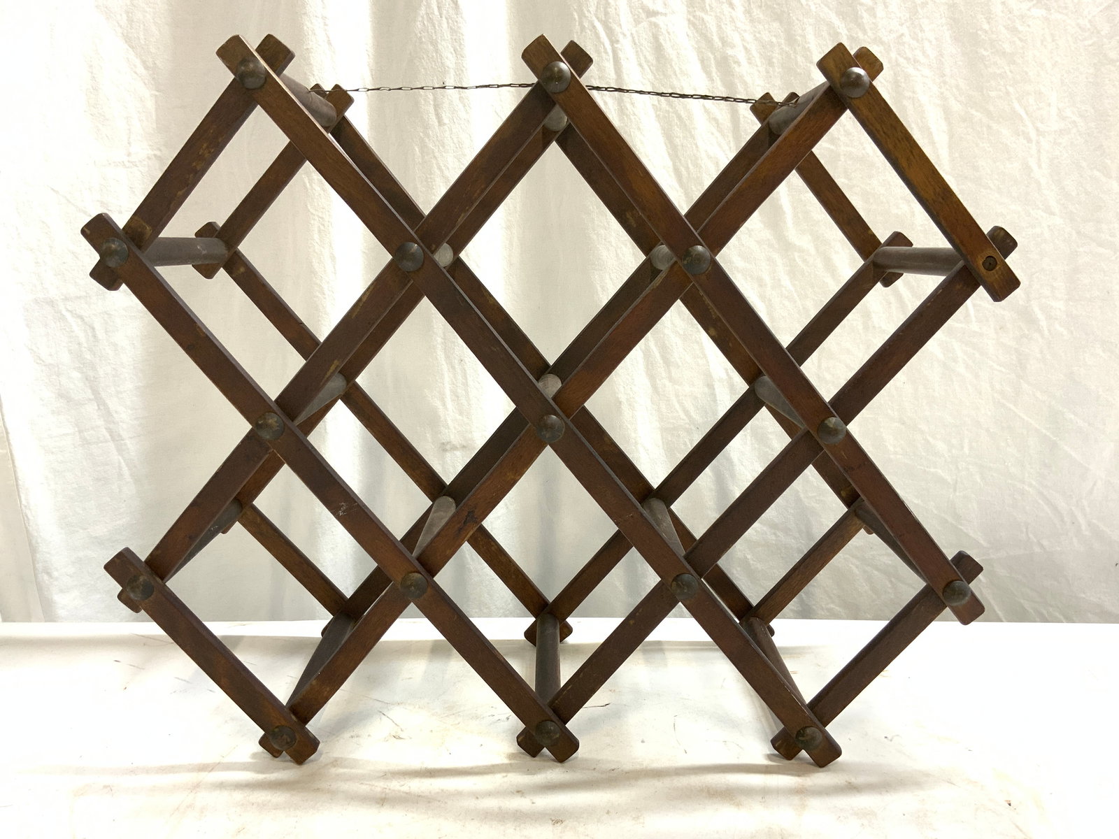 Vintage Folding Wooden Wine Bottle Rack: Wine bottle rack is vintage. Piece is brown toned and wooden. Rack has 8 bottle holding areas. Piece has diamond pattern shape. Bottle rack measures approximately 21 inches long 17.5 inches tall 7.5 i