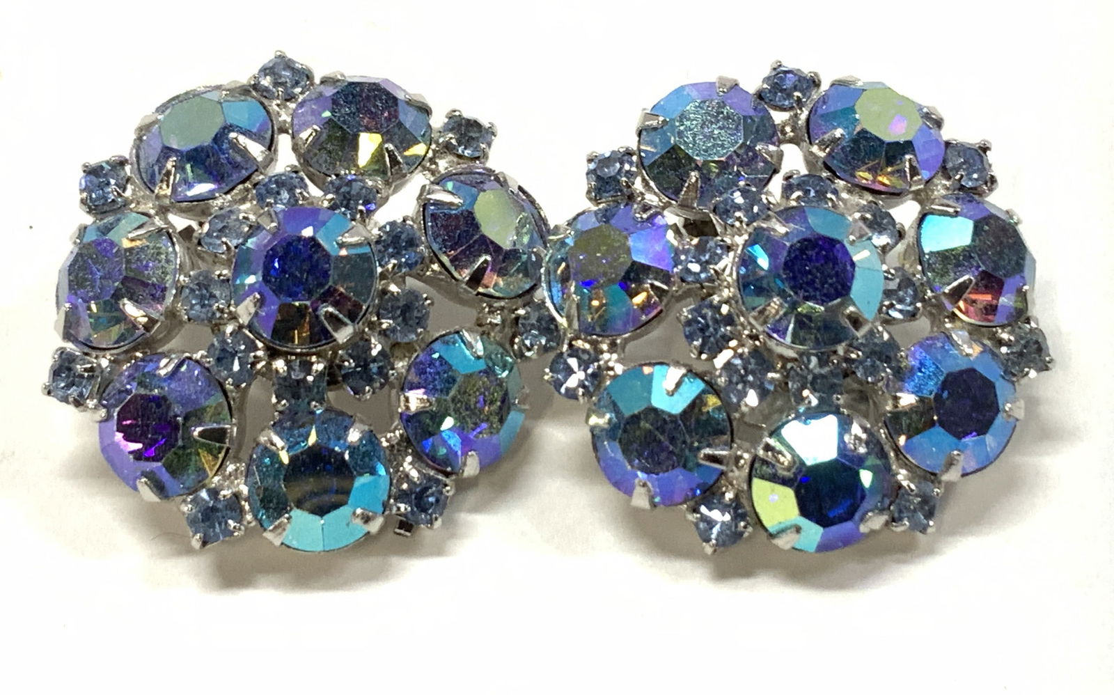 CARNEGIE Aurora Borealis Cluster Clip Earrings: 1.25 in. Round Aurora Borealis cluster clip on earrings with light blue crystals set in silver tone., brilliant iridescence. Signed Carnegie. Property of Manhattan estates and fashion industry executi