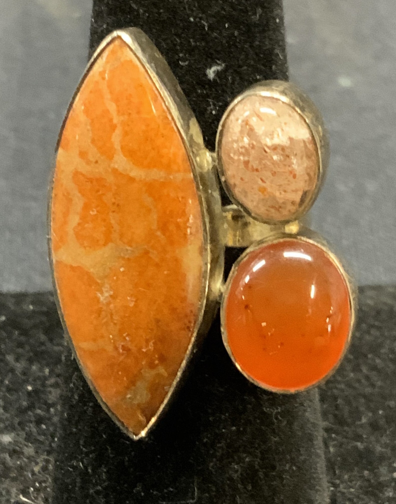Sterling Silver Orange Gemstone Ring: Sterling silver ring with orange toned gemstones. Marked 925. Adjustable band. Setting measures approx. 1.25 inches wide. Total weight 7.6 ozt. Some surface wear including scratching observed.