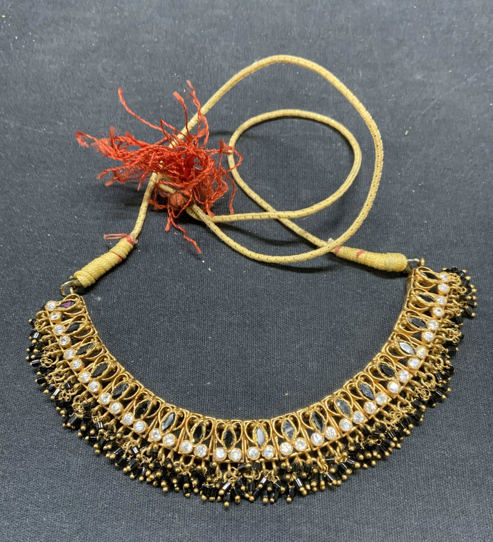 Vintage Gold Tone Crystal Necklace: Vintage gold tone necklace with black and colorless crystal decoration on cord. Drop length approx. 12 inches. Some surface wear including scratching observed. Some crystal may need replacement. Estat