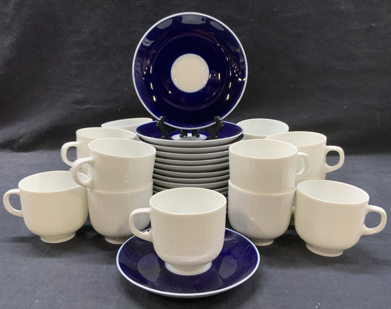 Set 31 Hutschenreuther Porcelain Cups & Saucers: Set of 30 porcelain saucers and cups, all marked Hutschenreuther. 15 White cups at 2.5 inches tall and 3 inch diameter and 16 blue toned saucers. Approx 5.5 inch diameter. Minor wearing to surfaces du