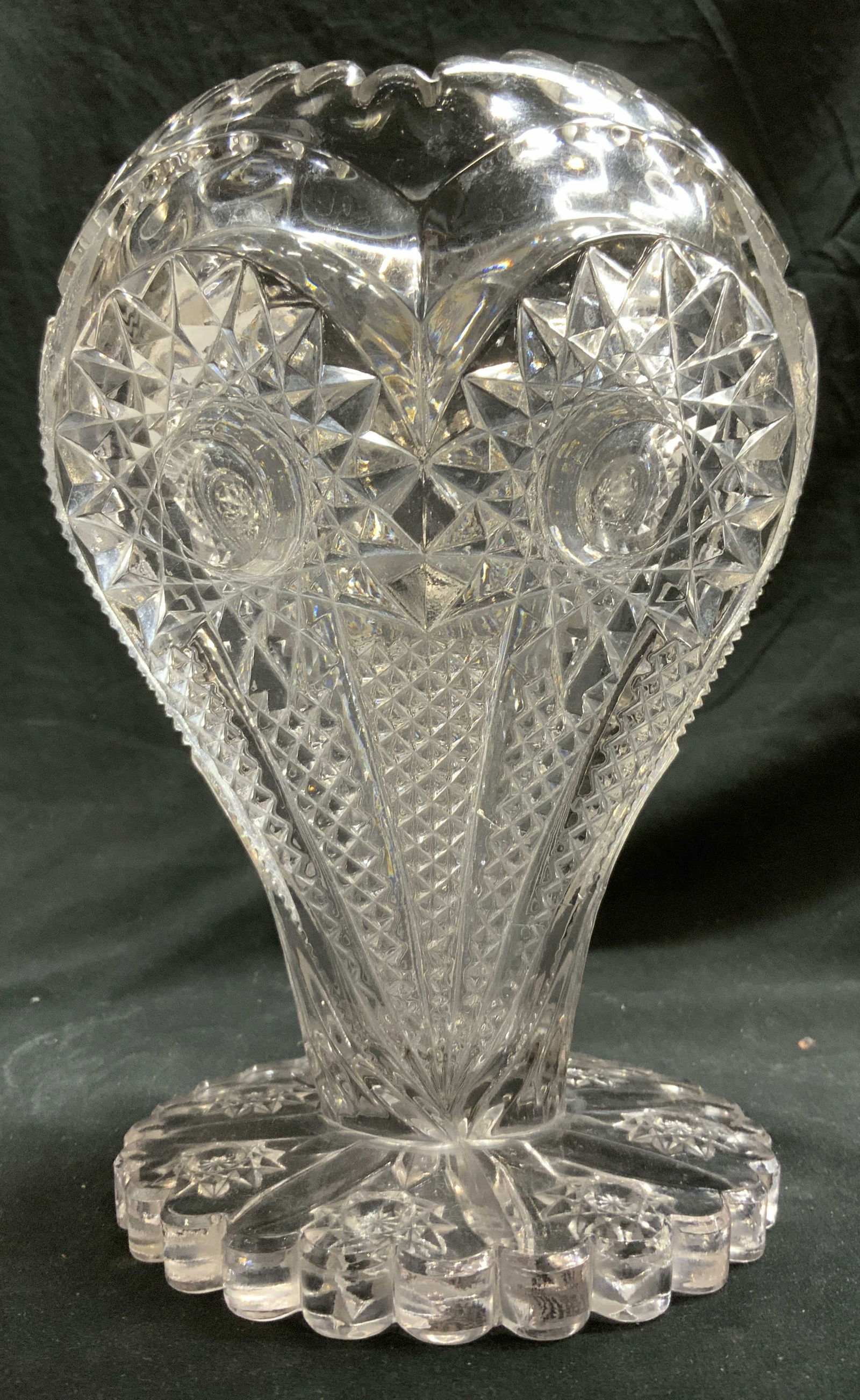 Footed Glass Owl Design Toothed Vase Vessel: Vase has toothed rim. Piece has detail on each side which resembles owl faces. Vase is footed. Piece measures approximately 8.75 inches tall 6.5 inches wide. Vase, vessel, footed vase, owl vase, tooth