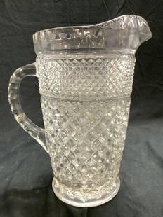 Footed Pressed Glass Pitcher Vessel: Pitcher has slight foot at base. Piece has diamond shaped relief detail. Vessel is glass. Piece measures approximately 9.75 inches tall 8.25 inches deep 5.5 inches wide. Pitcher, vessel, glass pitcher