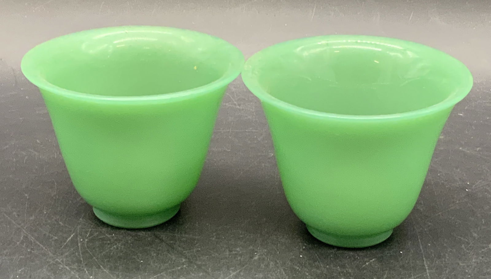 Pair Vintage Jadeite Glass Cups / Vessels: A pair of vintage Jadeite colored green glass cups / vessels. Slight flare to the rims. Pieces measures approx. 2.75H x 3.5W in. Some wear consistent with age and use. Collectibles, Vintage Jadeite Gl