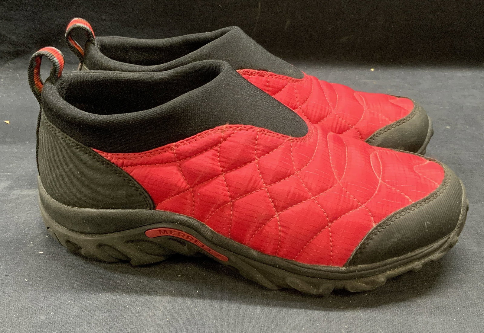 Merrell Red & Black Quilted Sneakers: Merrell red and black quilted slip on sneakers. Synthetic material. Size 7. Some wear to material and soles consistent with exposure. Merrell, Merrell sneakers, ladies designer sneakers, ladies design