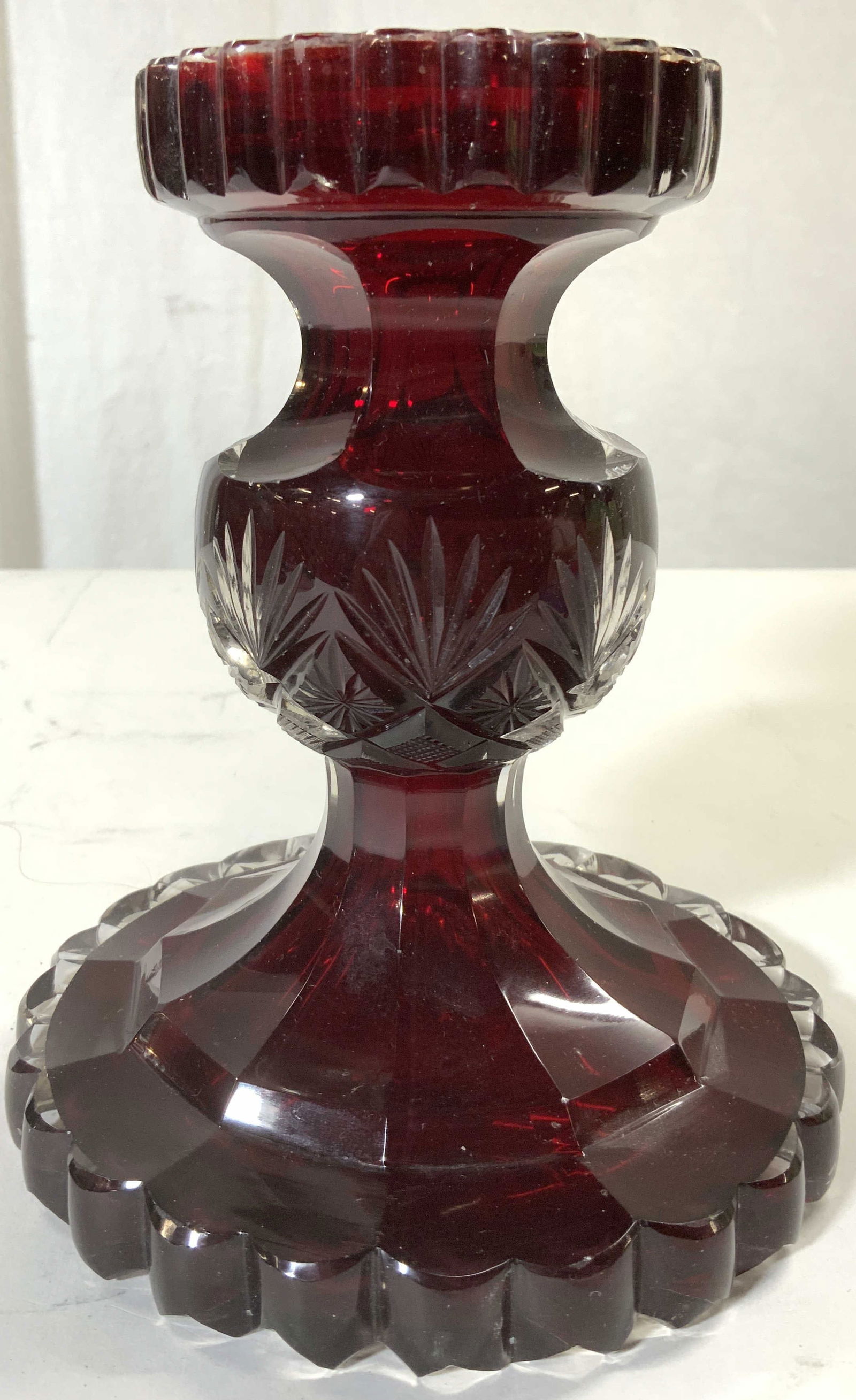 Cranberry Art Glass Candle Holder: Candle Holder is cranberry red toned. Piece appears to be crystal. Candle holder has geometric relief detail. Piece Measures approx 7 inches tall 5.5 inches wide. Candle holder, candlestick, crystal c