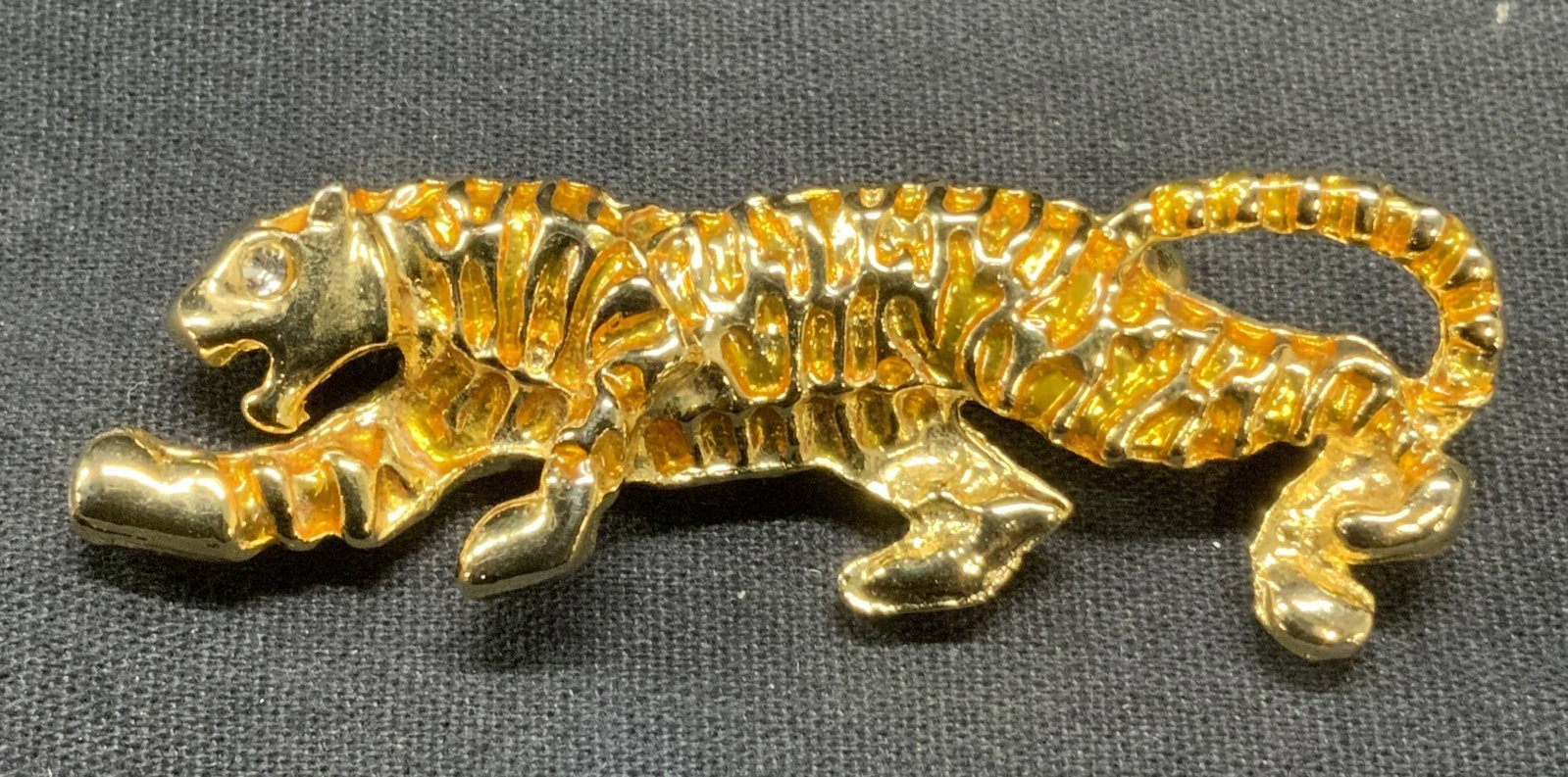 Vintage Gold Tone Crystal Tiger Brooch: Vintage gold tone tiger brooch with colorless crystal eye detail. Sculptural designer. Hinge pin to underside. Measures approx. 2.5 x .75 inches. Some surface wear including scratching observed. Prope