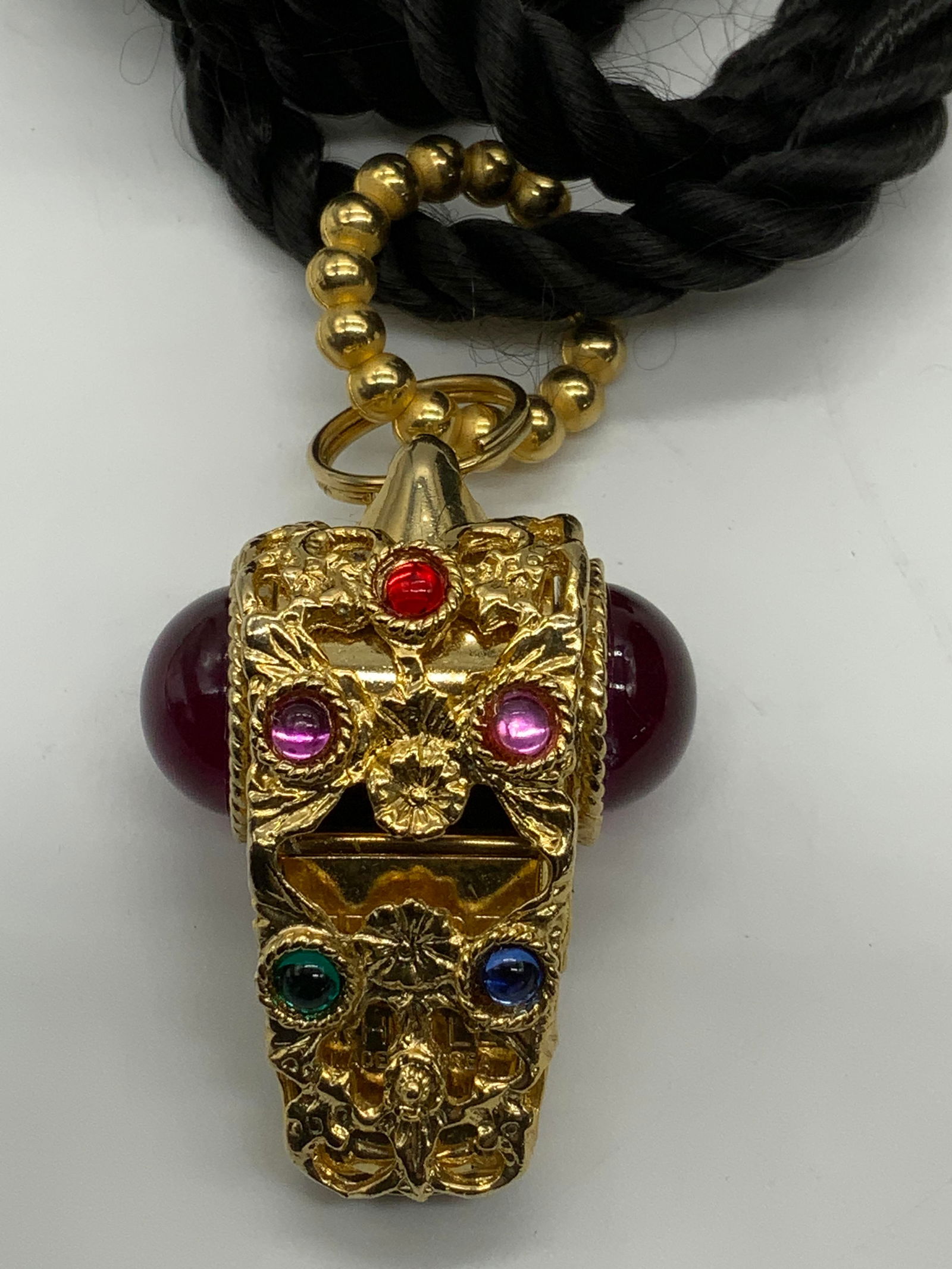 Vintage Gold Tn Bejeweled Whistle Necklace: Vintage gold tone bejeweled lucite Cabochon whistle pendant on black twisted cord. Drop length approx. 19.25 inches. Whistle measures approx. 1.5 x 1.75 inches. Some surface wear including scratching