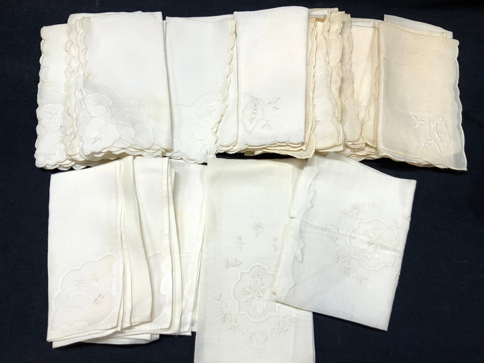 Lot 23 Vintage Embroidered Linens: Lot of 23 assorted sets of vintage linens, all with embroidered scroll or floral designs. Set of 12 linens with leaf embroidery. At 13.5 x 14 inches. Set of 6 with scalloped edges and scroll designs a