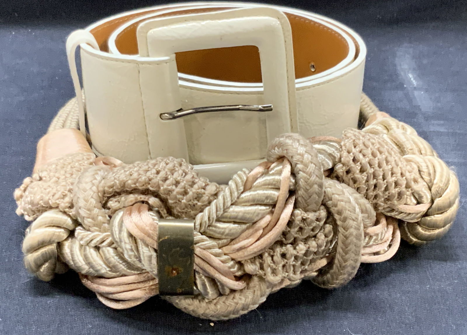 2 Leather & Woven Fabric Belts: Lot 2 belts. 1 white toned leather belt marked Luxuriously. Size 27. At 29 inches long and 2 inches wide and 1 woven fabric and rope belt with hooked clasp. Approx 29.5 inches long. Moderate wearing t
