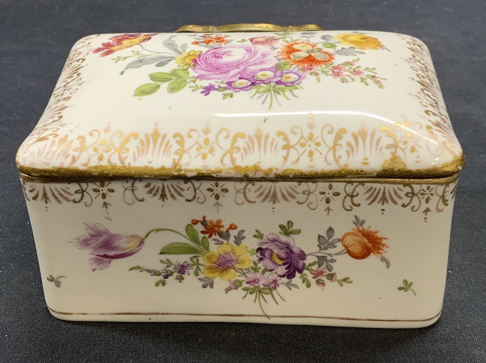 Trademarked Vintage Gilt Porcelain Floral Box: Vintage, possibly antique, gilt porcelain box with hand painted floral motif. Metal hinge. Trademarked with Crown above D. Measures approx. 5 x 3.5 x 2.5 inches. Some surface wear including scratching