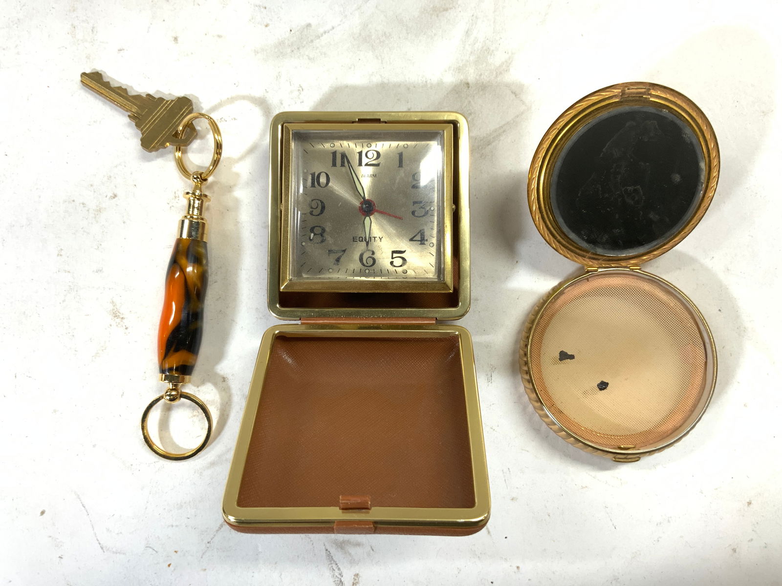 Lot 3 Keychain, Equity Clock, & Makeup Mirror: Lot includes 1 clock trademarked EQUITY, 1 makeup mirror, & 1 enameled keychain with key. Clock when fully open measures approximately 6 inches long 2.75 inches wide. 2.75 inches square when closed. K