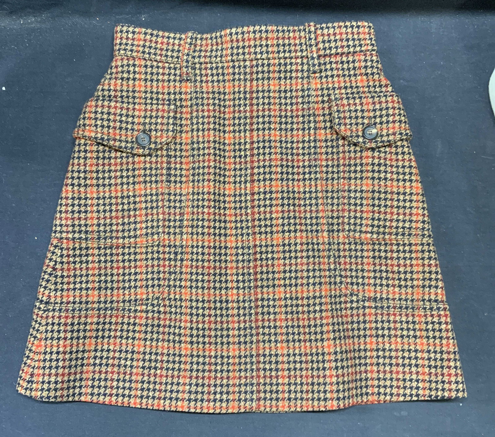 Prada Tan Wool Hounds Tooth Skirt, Italy: Prada tan, red, and black houndstooth skirt. Belt loops on waist and 2 side pockets with buttons. Hidden back zipper closure. Size 38. 90% wool 10% polyamide. Made in Italy. Gently worn. Prada, Prada 