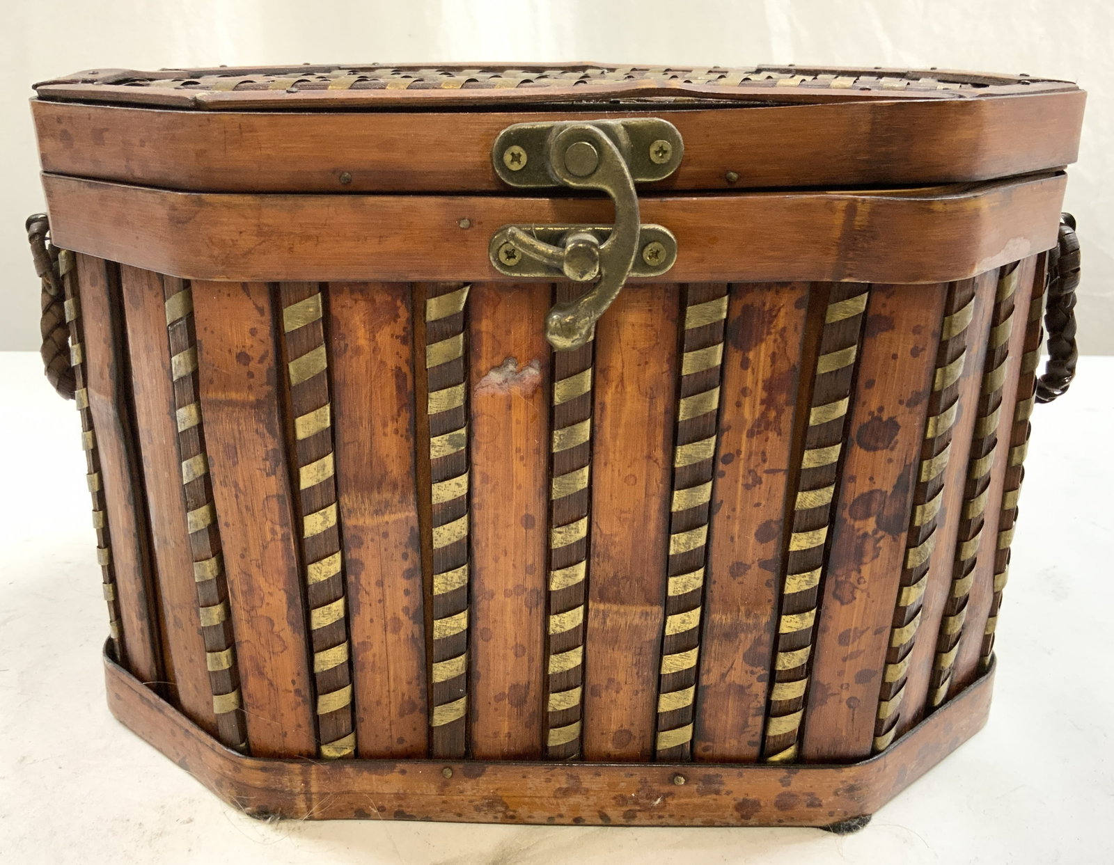Vintage Lidded Wooden Chest W Brass Lock: Chest is vintage. Piece appears to be wooden. Chest has hinged lid. Piece has gold toned brass locking mechanism. Chest has woven handles at sides. Piece measures approximately 11.5 inches wide 7.5 in