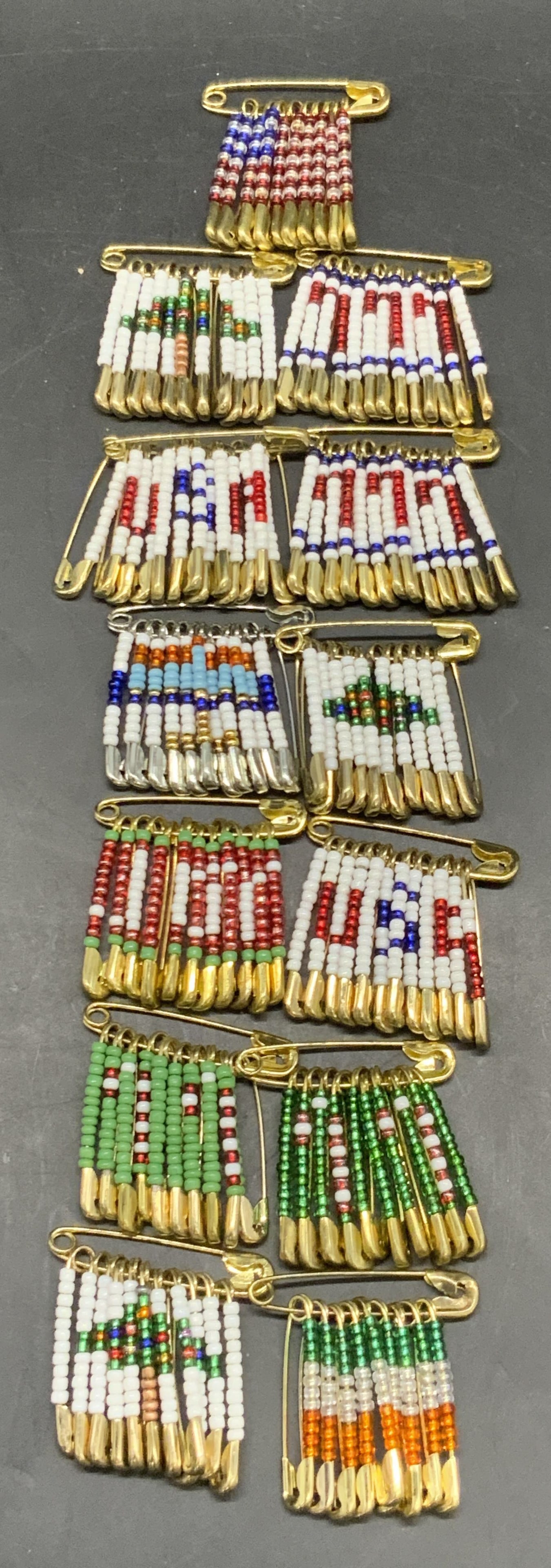 Lot 13 Seed Beaded Safety Pin Brooches: Thirteen seed beaded safety pin brooches. Gold and silver tone metal safety pins decorated with multicolored seed beads. Pieces are similar in size, one measures approx. 1.5L x 1.5W in. Some wear cons