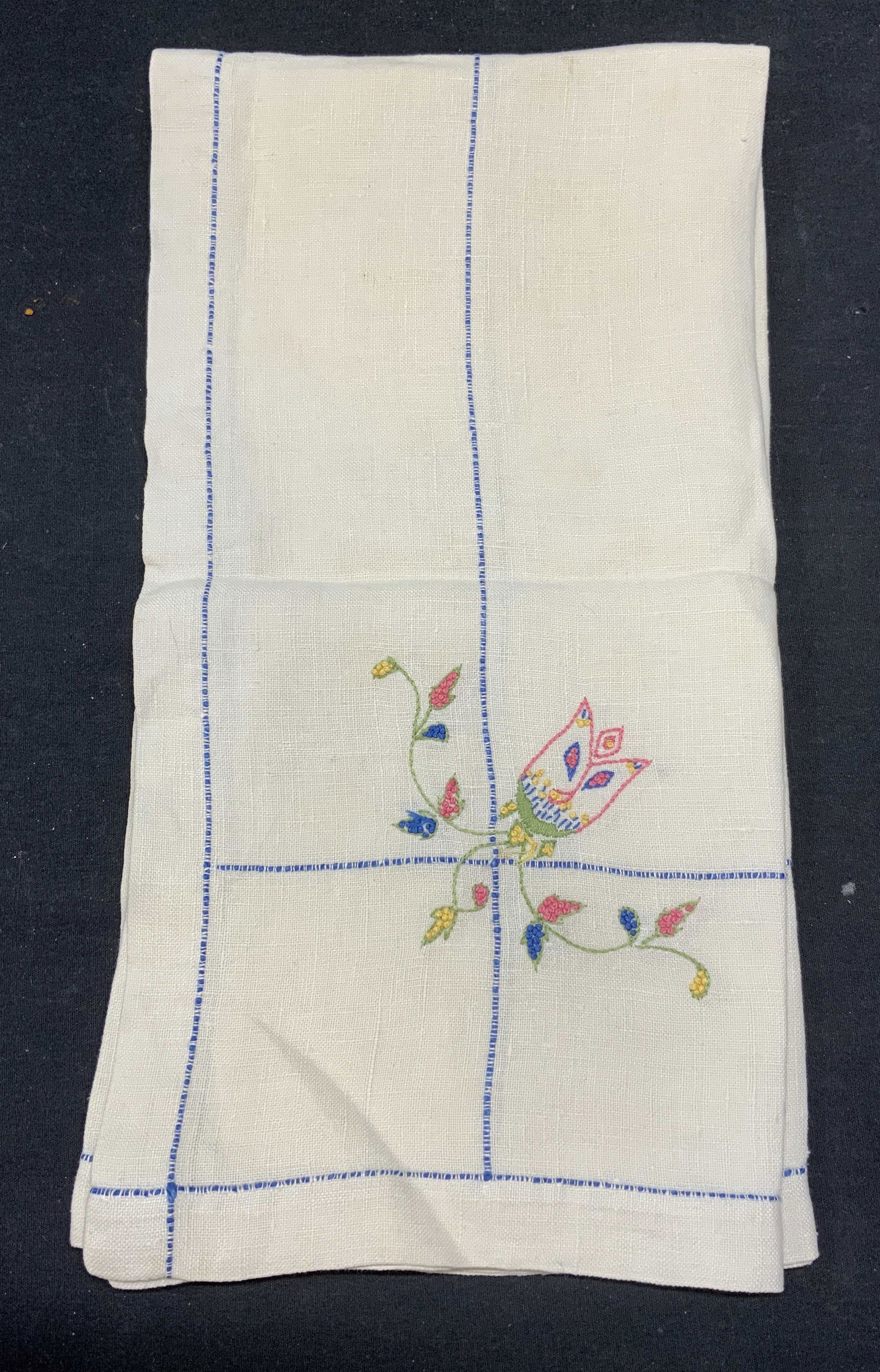 Vintage Embroidered Linen Floral Tablecloth: Vintage square shaped embroidered linen tablecloth in white with blue trim and pink, green, and yellow flower motif. Measures approx. 32.5 x 32.5 inches. Some wear to material and blemishes consistent