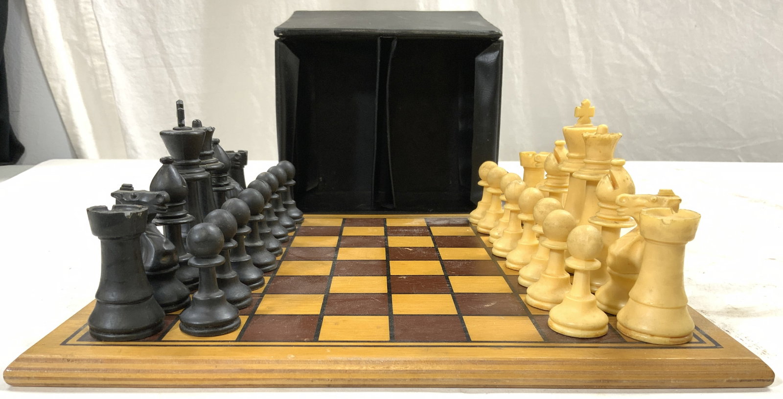 Lot 33 Wooden Chessboard, Game Pieces & Case: Lot includes 1 chessboard & 32 game pieces. Lot includes all chess game pieces and wooden board. Includes black and tan toned pieces. Case is trademarked REALISTIC. Board has tan, brown and black tone