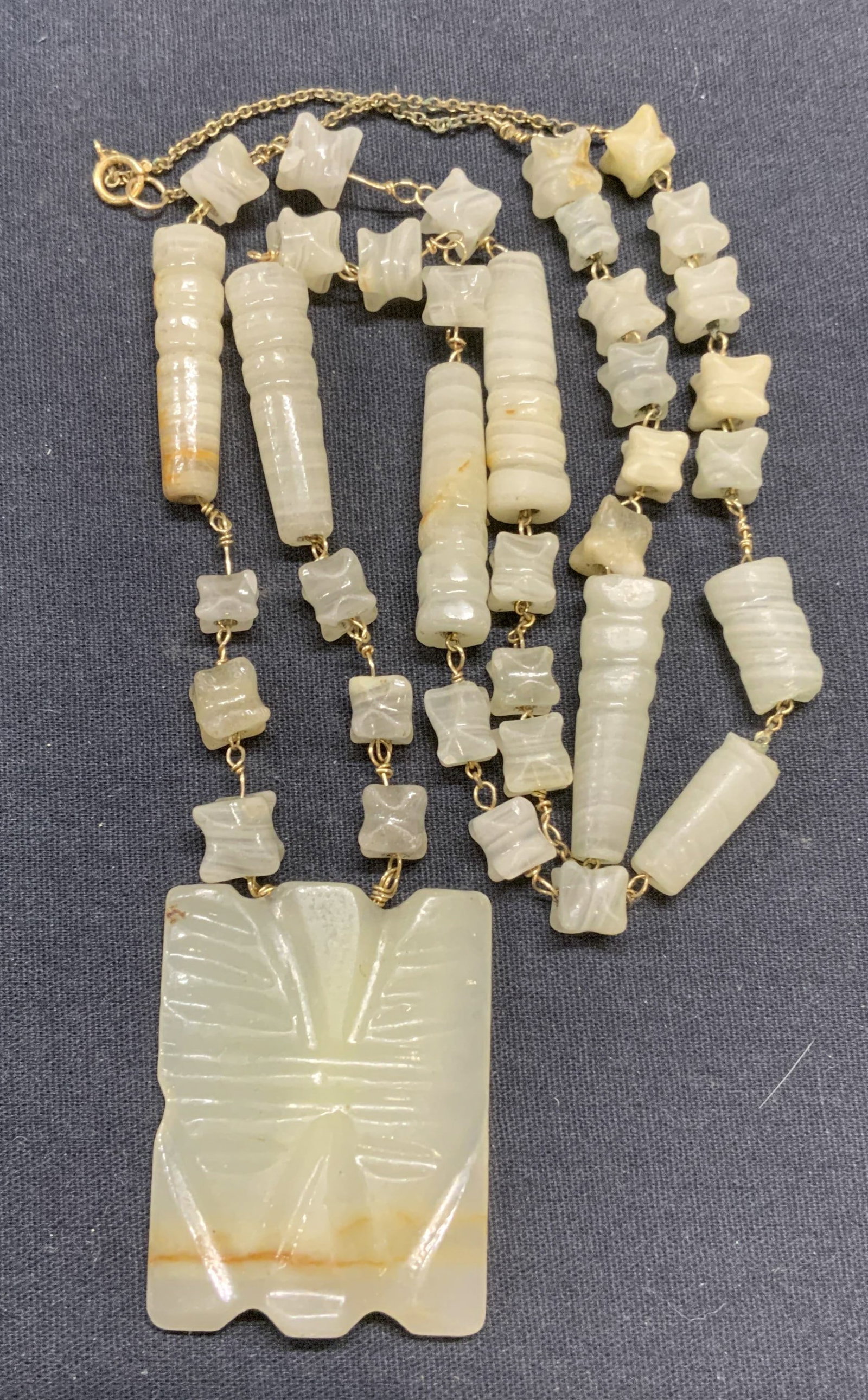 Gold Tone Natural Stone Pendant Necklace: Gold tone necklace with opaque pale green banded natural stones. Possibly carved onyx. Drop length approx. 14.25 inches. Pendant measures approx. 2 x 1.5 inches. Some scratching observed. Estate jewel