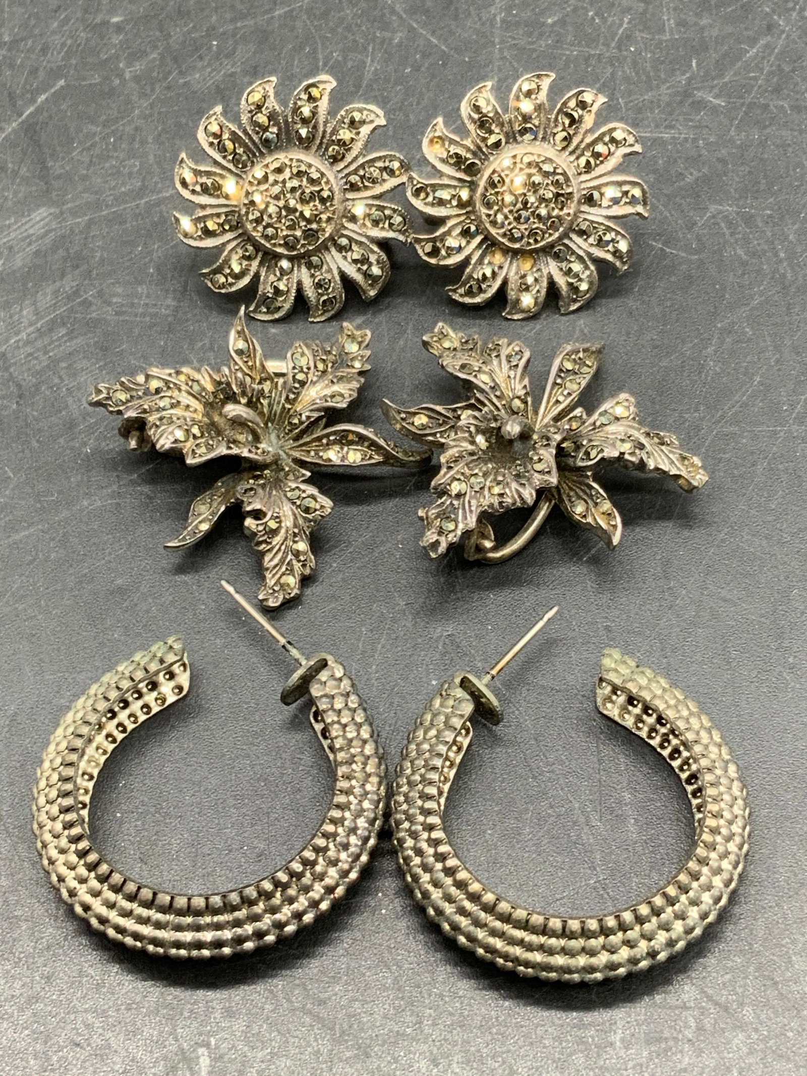 Lot 3 Platinin, Sterling Silver, & Silver Tn Earrings: A lot consisting of three pairs of vintage earrings. Sunflower form earrings studded with marcasite read STERLING to screw backings. Total weight .36 ozt. Art Deco Iris form earrings studded with marc