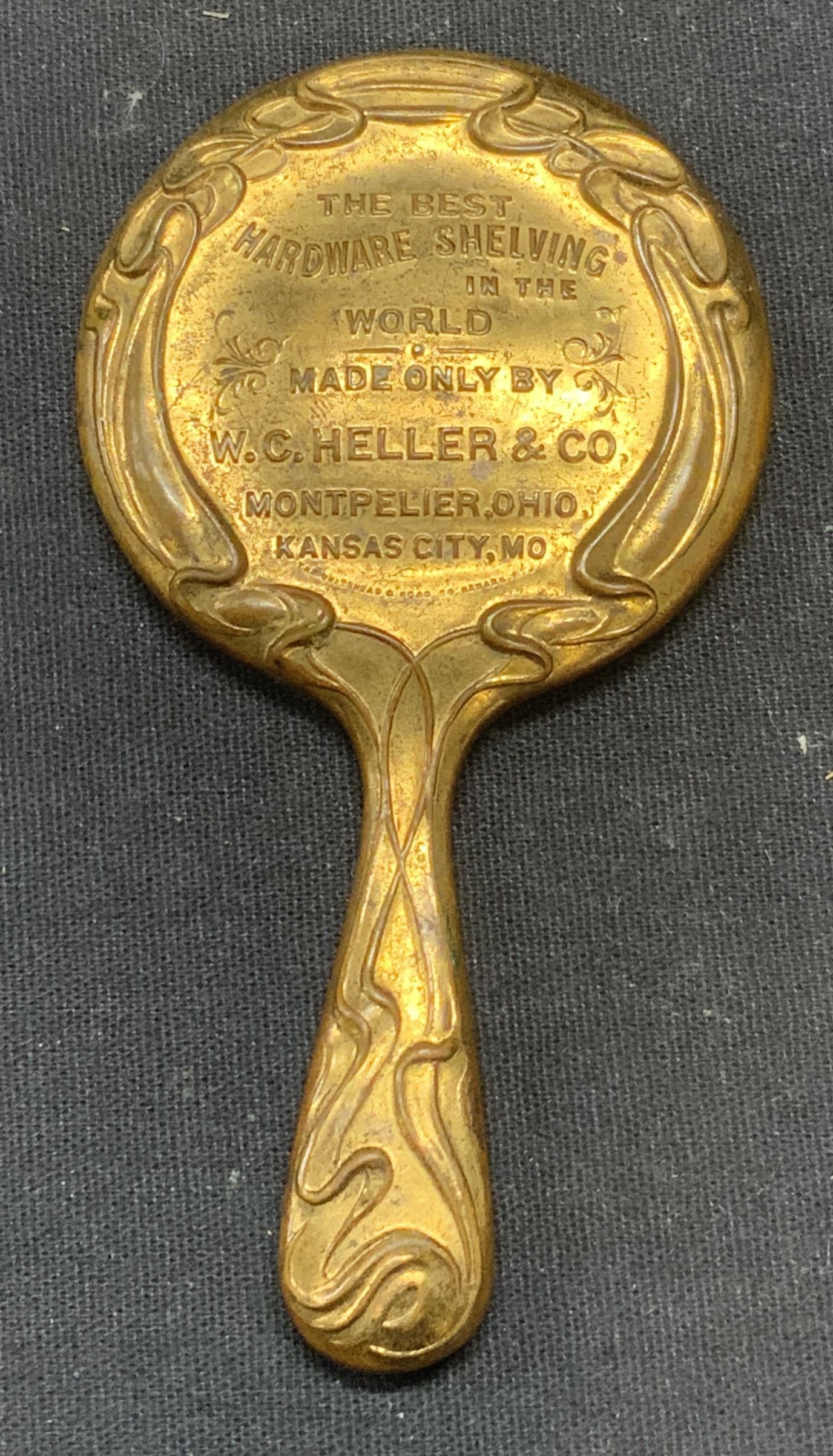 Vintage Brass Advertising Hand Mirror: Vintage brass advertising hand mirror with ornate embossed scroll. Reverse reads The Best Hardware Shelving in the World Made Only By W. C. Heller & Co. Montpellier, Ohio, Kansas City, Missouri. Measu