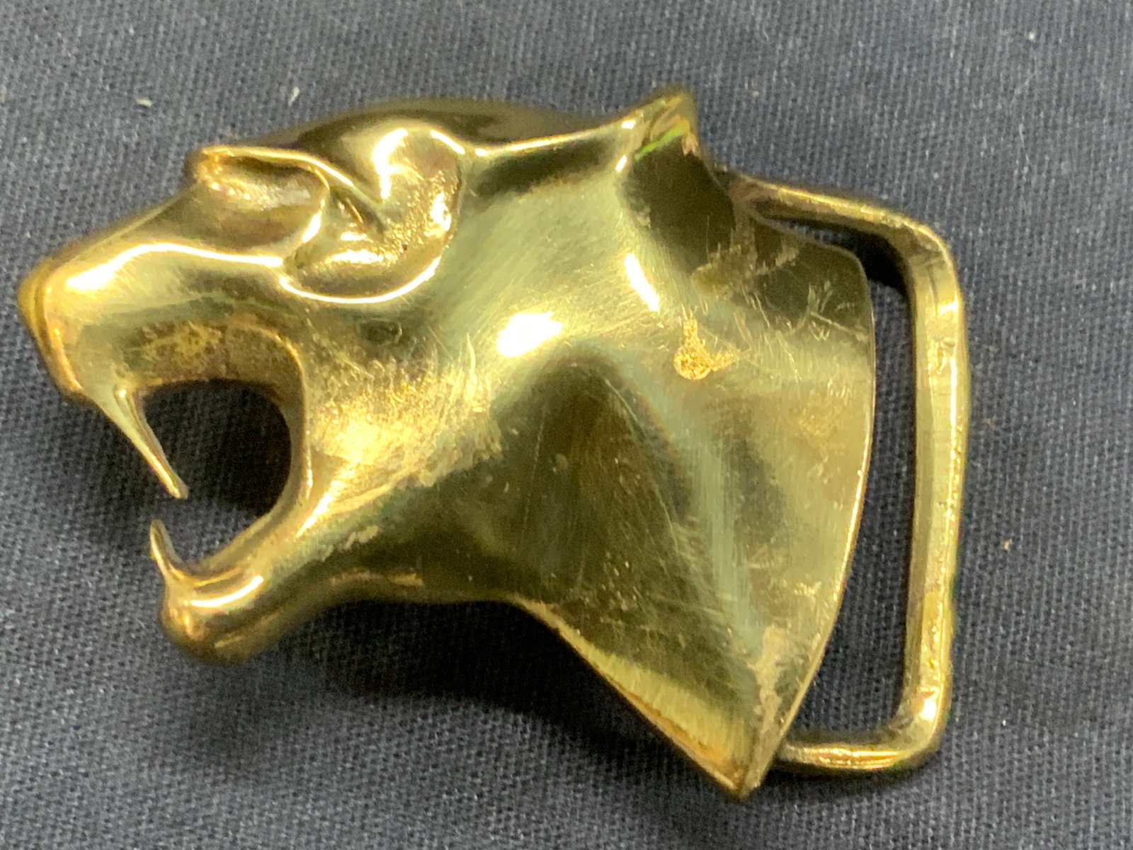 Vintage Cast Brass Omega Puma Head Belt Buckle: Vintage cast brass belt buckle, in the shape of a pumas head, stamped on backside with an Omega symbol approx 2.5 inches wide and 1.75 inches long. Moderate wearing to brass due to age and use. Brass 