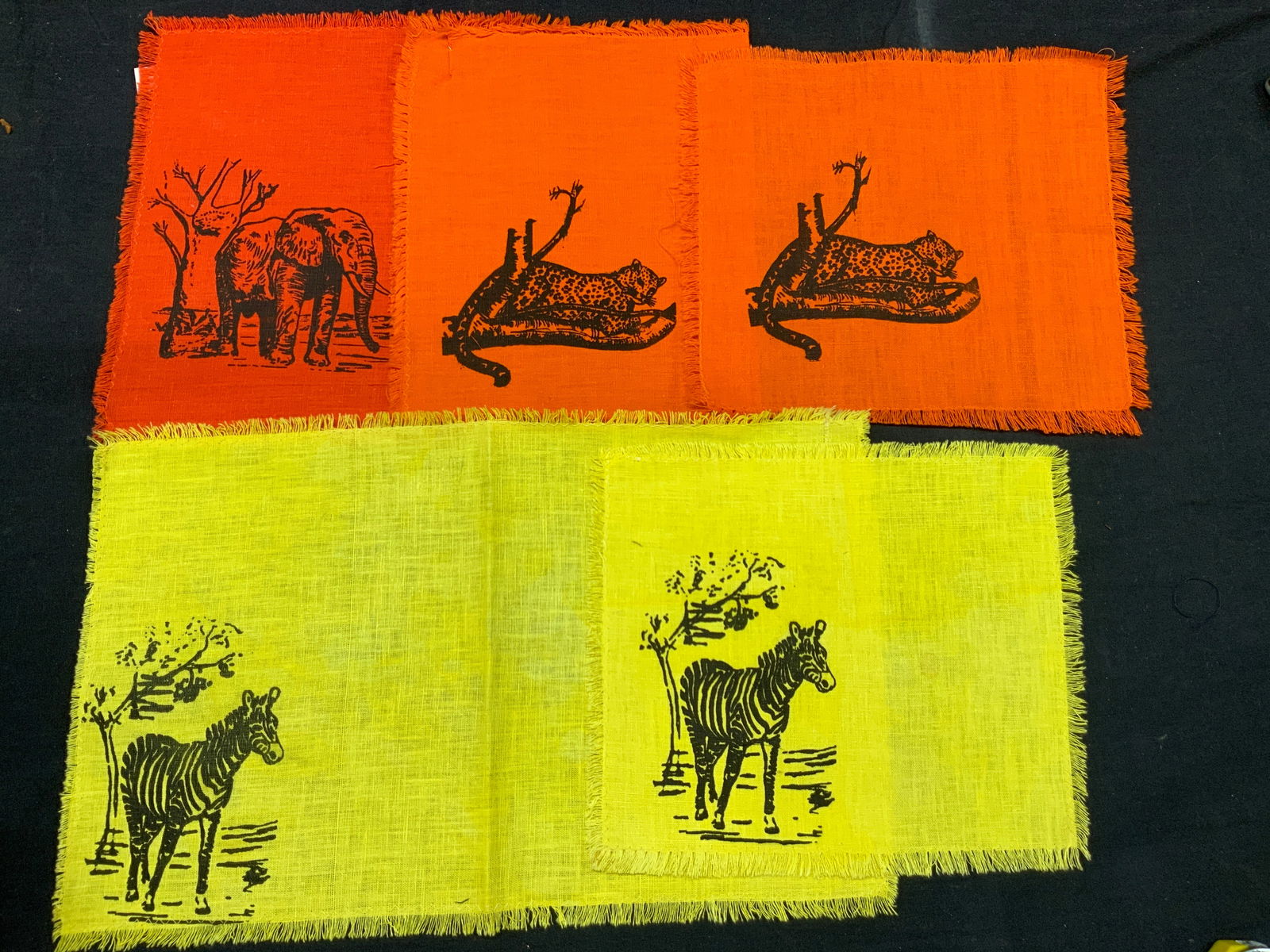 Lot 5 Wild Animal Elephant Graphic Linens: Lot of 5 table linens. 1 red with an elephant motif, at 10 x 18 inches. 2 orange toned linens with leopard motifs 10 x 16 and 10 x 9 inches and 2 yellow toned liens with zebras, approx 10 x 16 and 10