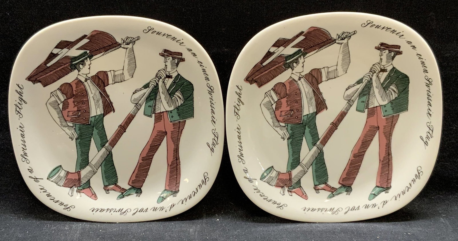 Pair Porcelain SwissAir Kurt Wirth Souvenir Plates: Pair of porcelain SwissAir souvenir plates. Figures with horn and Swiss flag, Designed by Kurt Wirth, produced by Porzellanfabrik Langenthal. Measure approx. 6 x 6 inches. Some surface wear to each in